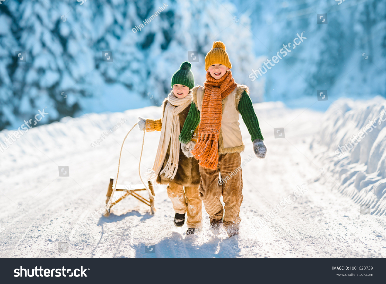 Two little kids have fun in the beautiful winter nature with snow-covered trees. Children walk along a snowy road pulling a sled. Winter knitted wool retro clothes.