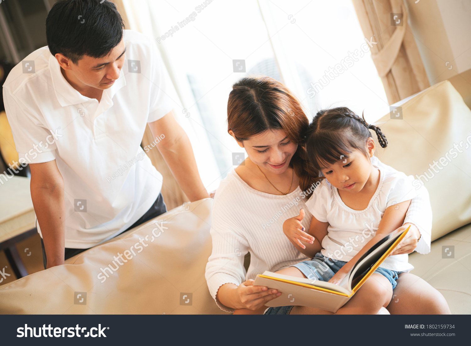 Asian mother reading book to her daughter at home during home schooling 