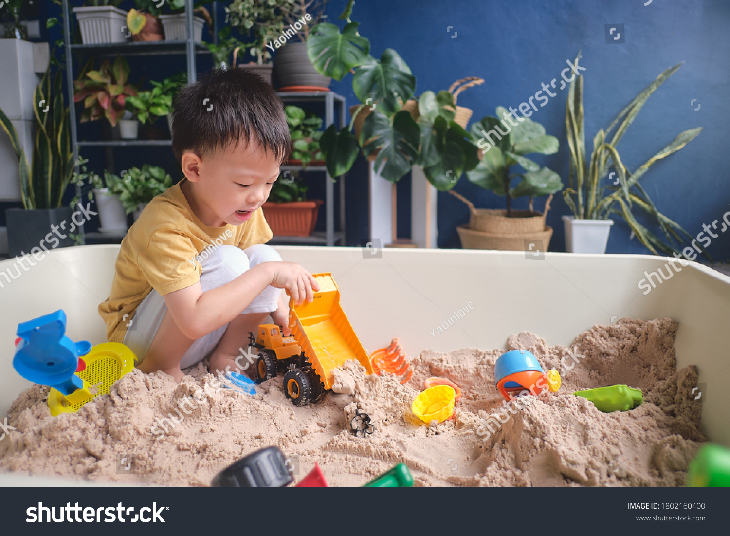Cute Asian young boy playing with sand alone at home  Kid playing with sand toys & toy construction machinery in urban home garden   Montessori education  Creative play for kids concept