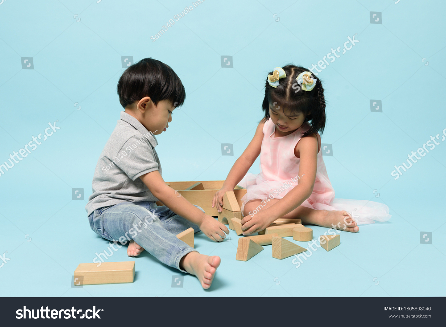 Asian two people kids playing together to be enjoyable with wooden toys block on pastel blue background in studio. Skill of children  Childhood roles and Birth order  Child development concept.