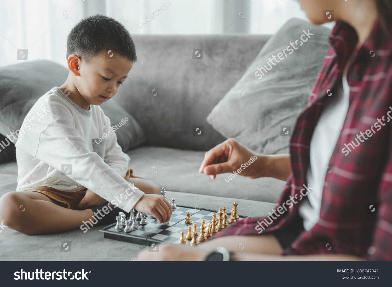 Family hobbies. son playing chess with mother at home. Little boy engaged in board game with his parent in room. Asian people.
