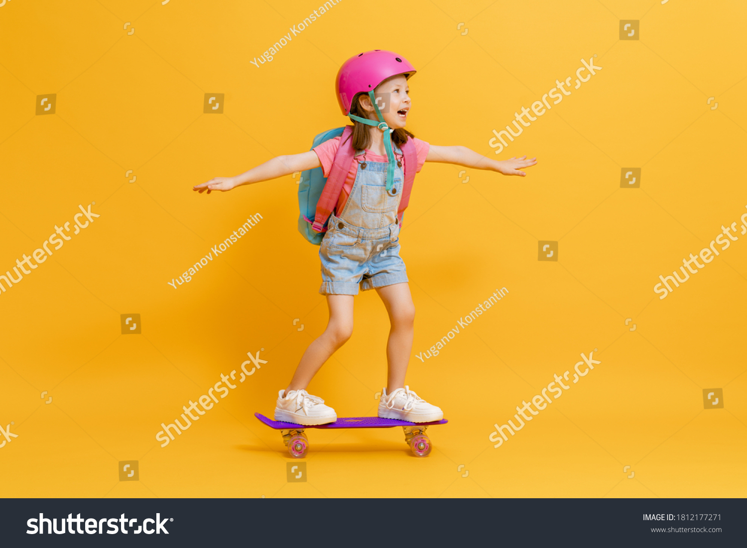 Childhood and happy time! Cute child with skateboard on color paper wall background. Kid with backpack. Girl ready to study.