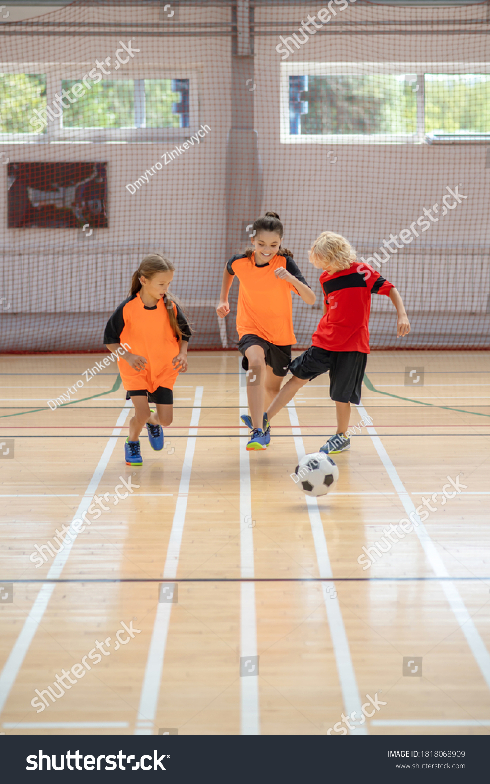 Football. Three kids in sportswear playing indoors football in the gym