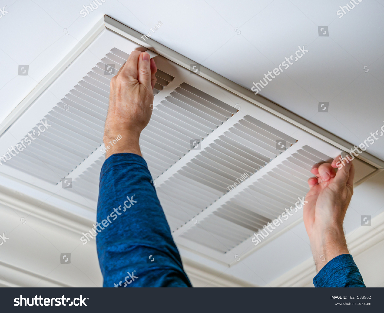 Man opening ceiling air vent to replace dirty HVAC air filter. Home air duct system maintenance for clean air.