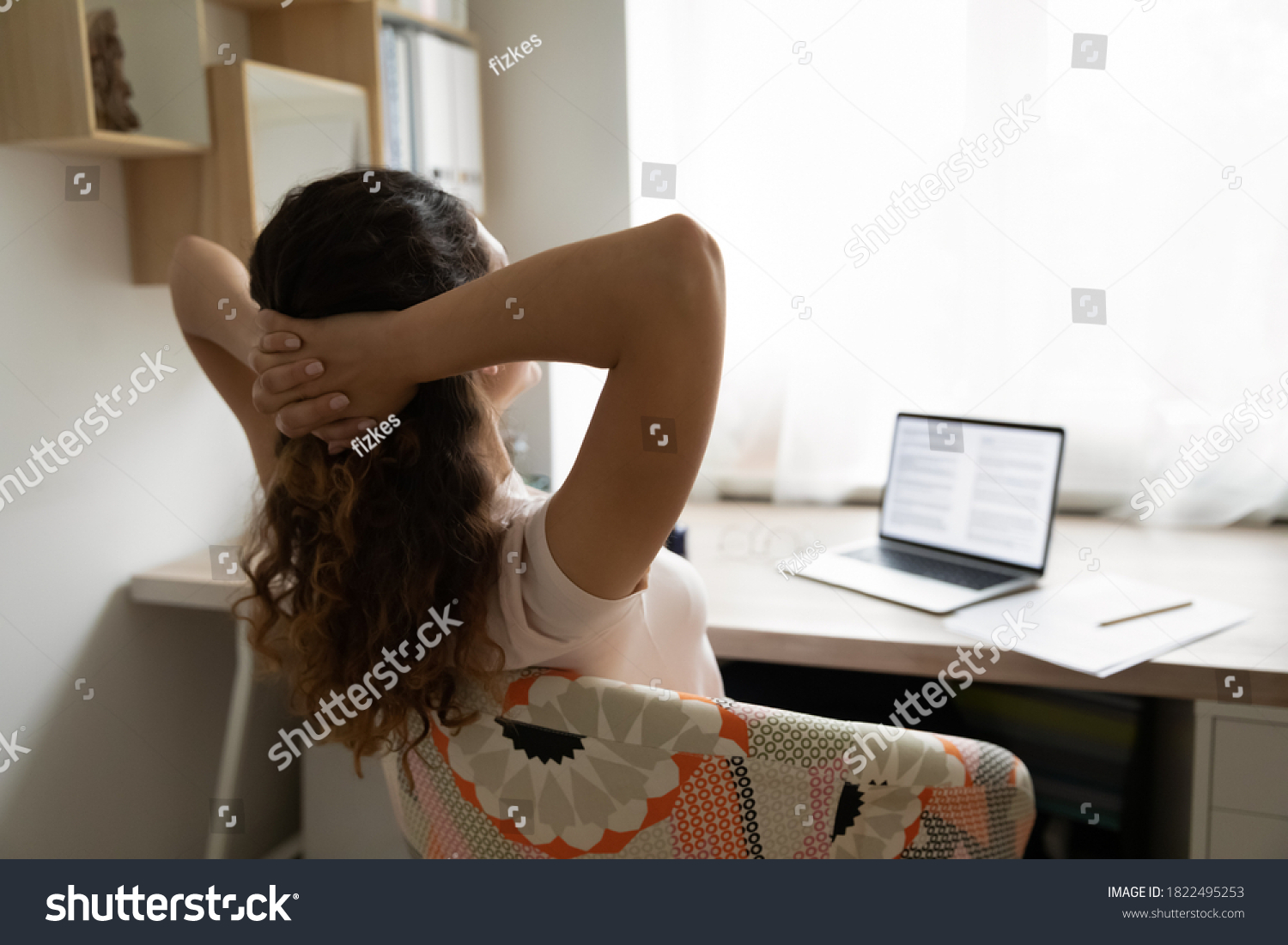 Rear view of relaxed young woman sit rest in chair working online on computer in home office. Exhausted female relax at workplace relieve negative emotions breathe fresh air. Stress free concept.