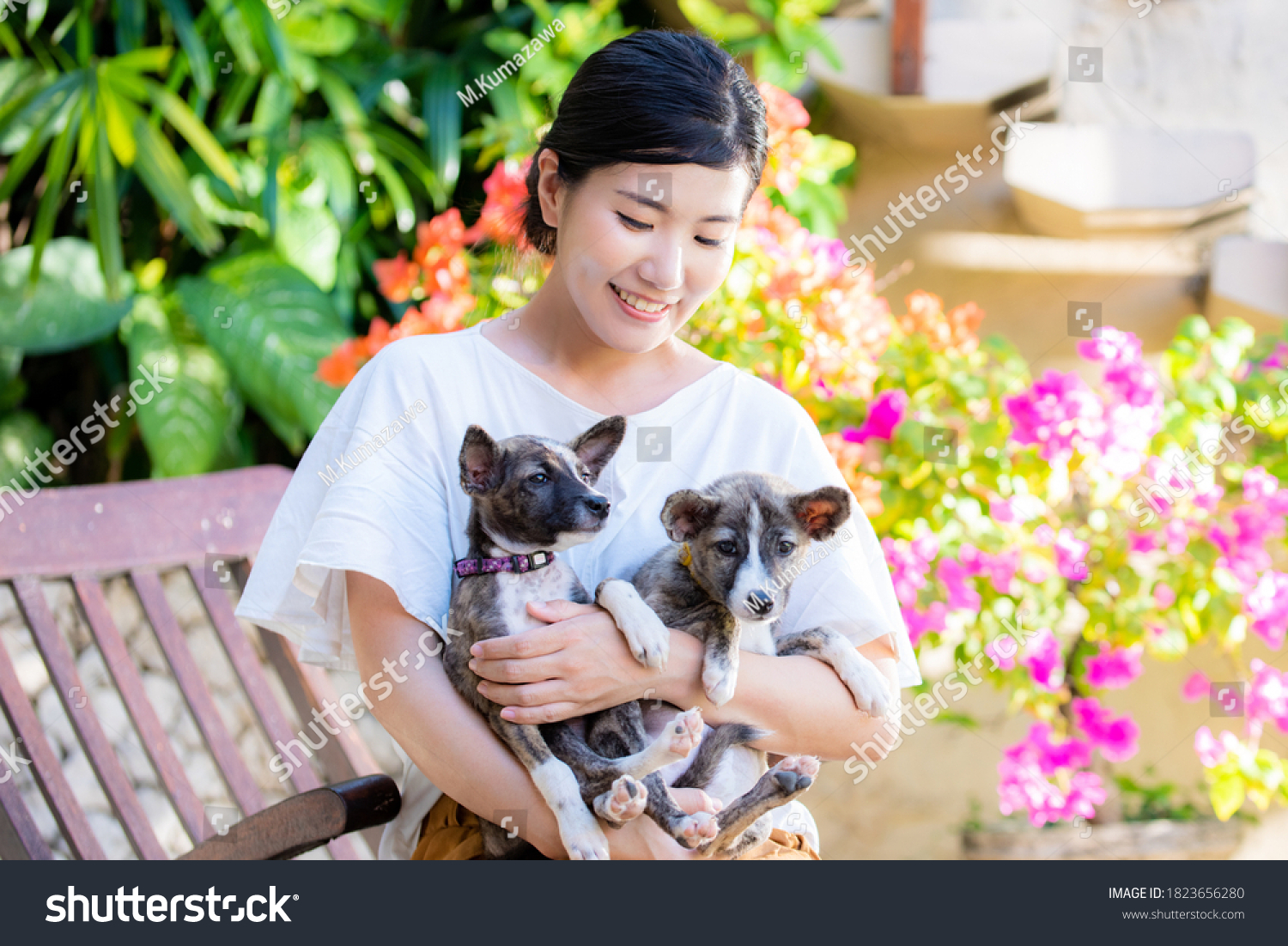 A Japanese woman holding two cute puppies in a colorful garden