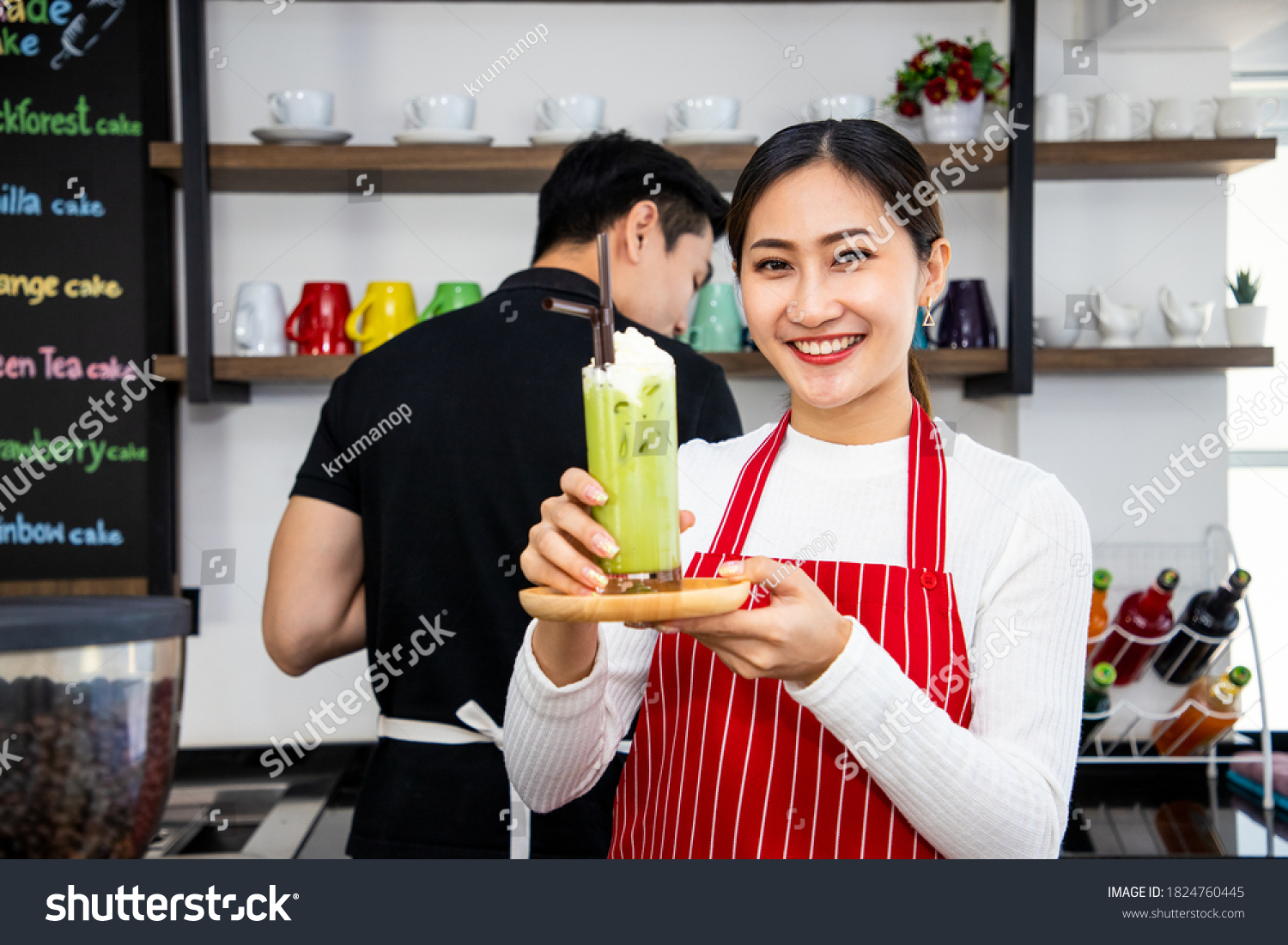 Beautiful barista holding out a glass of iced tea. Matcha green tea drink in a glass with milk cream. Useful latte. Vintage tone and soft focus