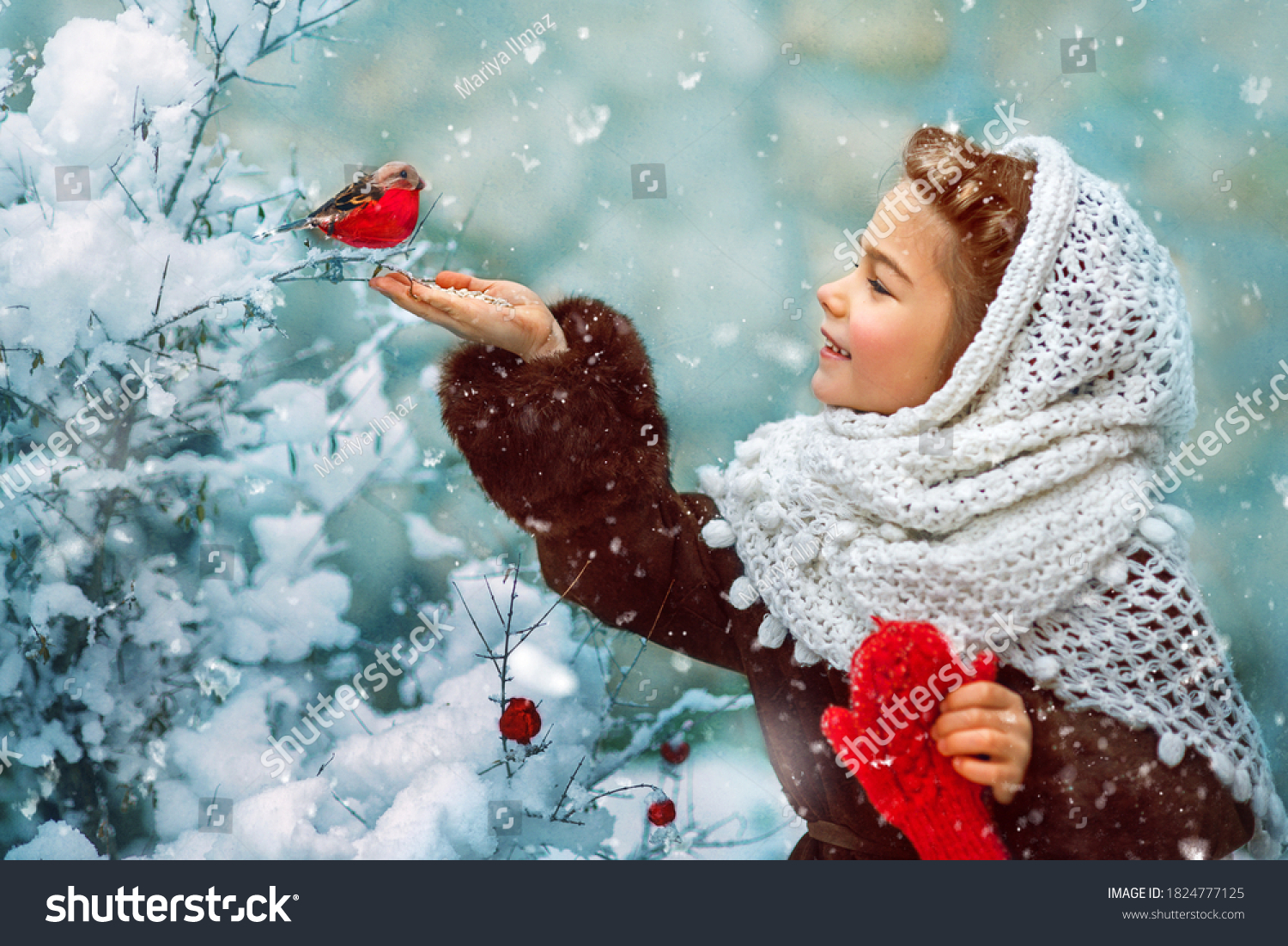 Photo as a postcard in vintage style depicting a small girl in a white downy shawl and red mittens  smiling and feeding a bullfinch bird from her hand  while white fluffy snow is falling around.