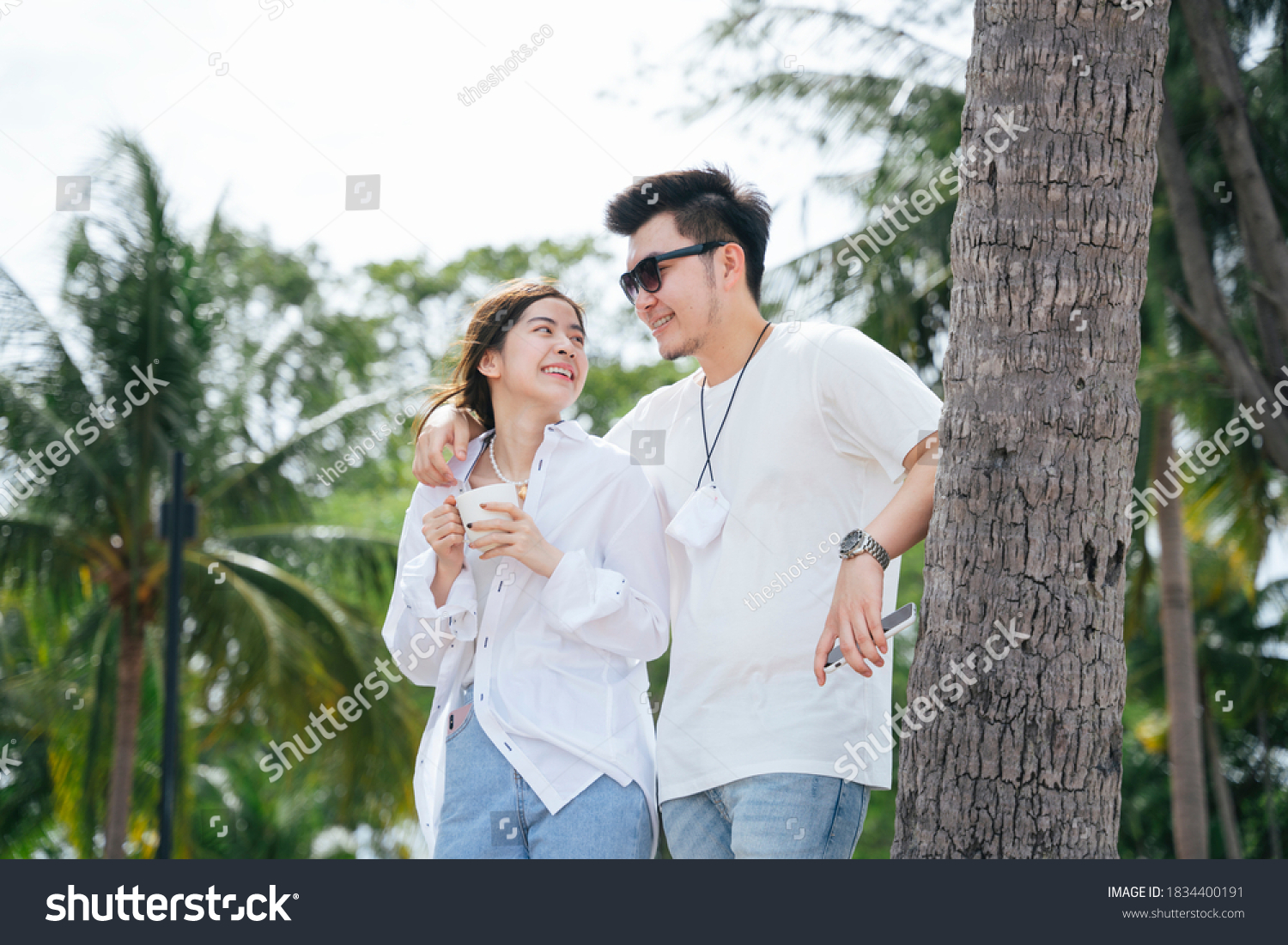 Asian couple traveler holding shoulder standing on the beach near coconut tree.