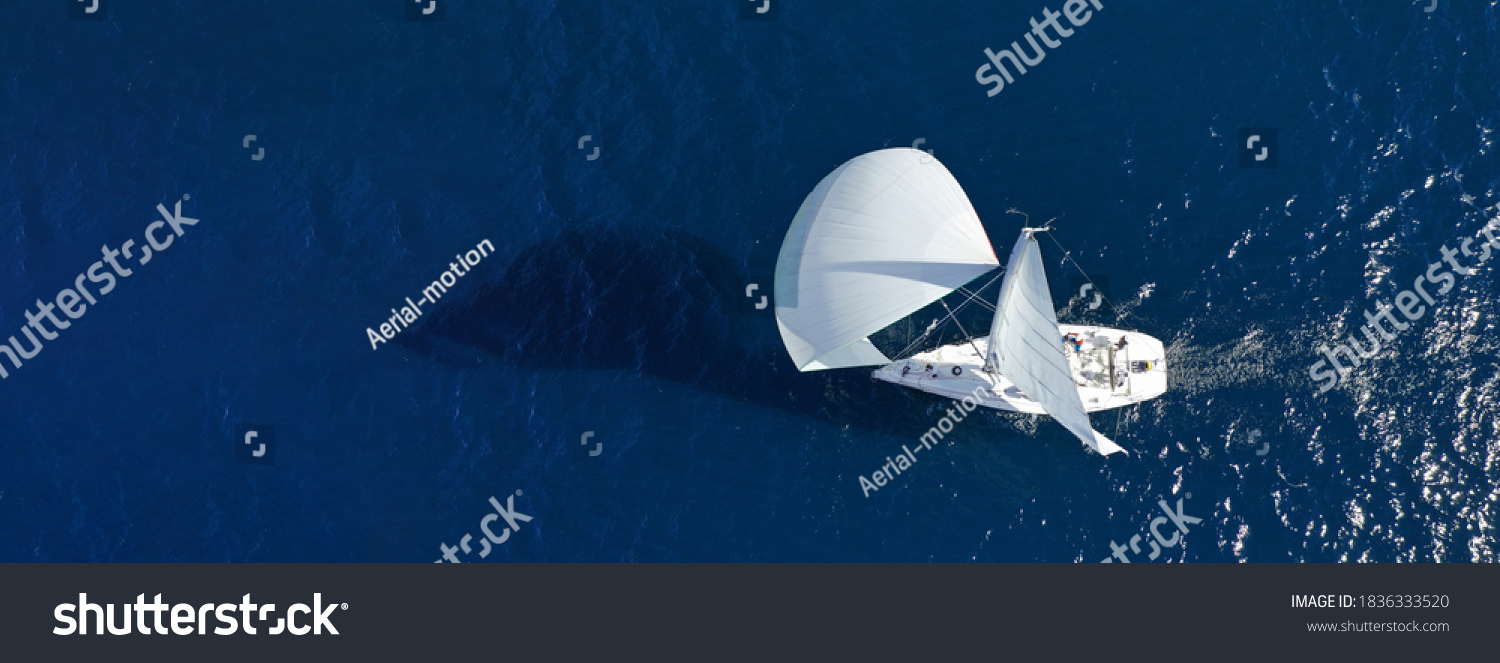 Aerial drone ultra wide panoramic photo of beautiful sailboat with white sails cruising deep blue sea near Mediterranean destination port