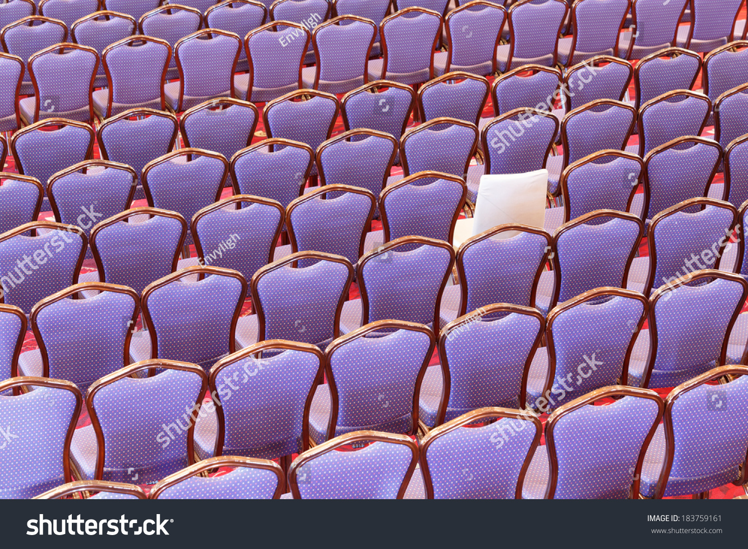 Entertainment background with rows of vacant seating in an auditorium with purple upholstery except for one different seat in cream in a concept of individuality and diversity
