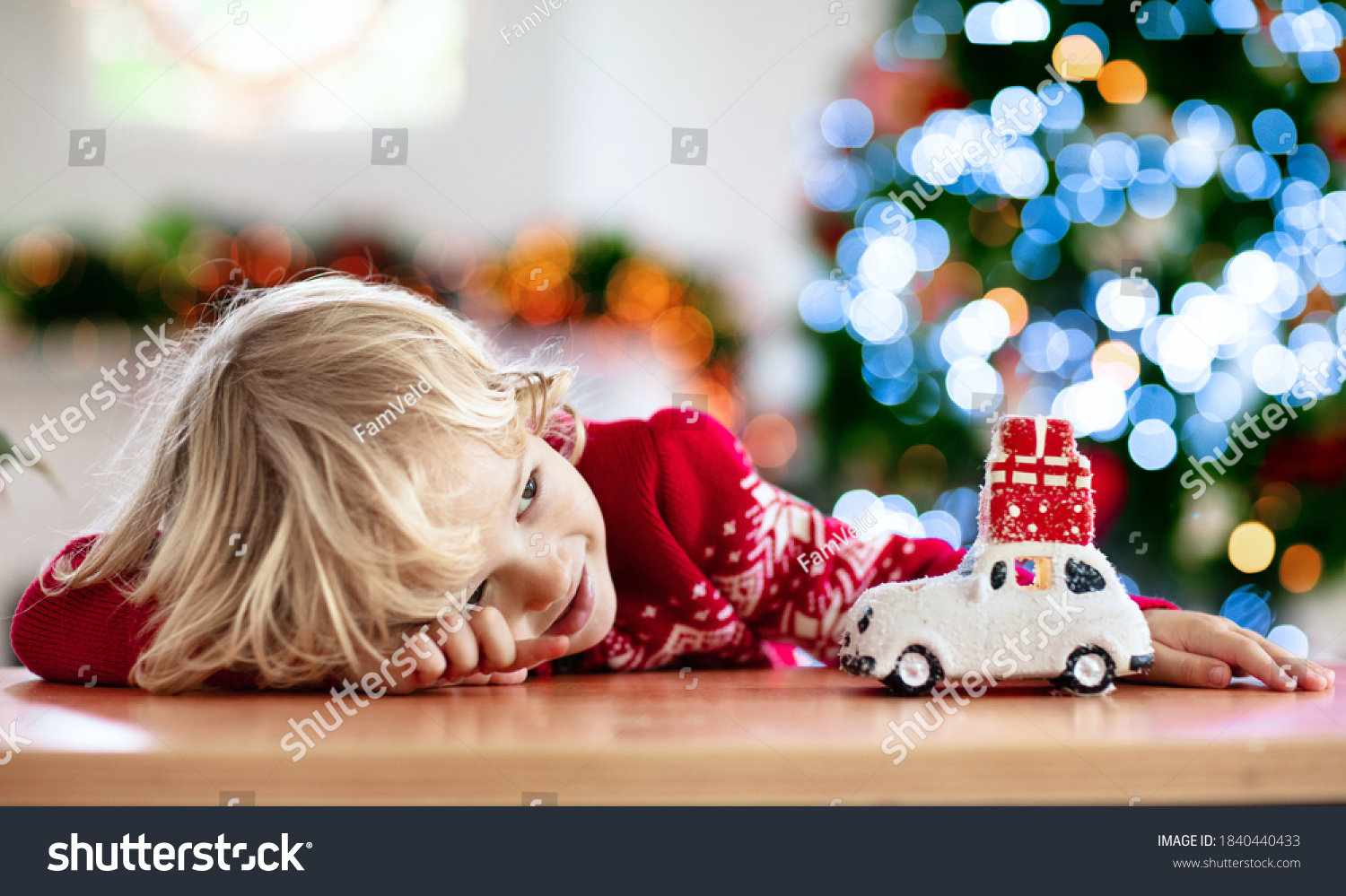Child with Christmas present. Kid with Xmas gift. Little boy playing with a toy car under Christmas tree. Decorated home for winter holidays. Celebration with children. Kids play.