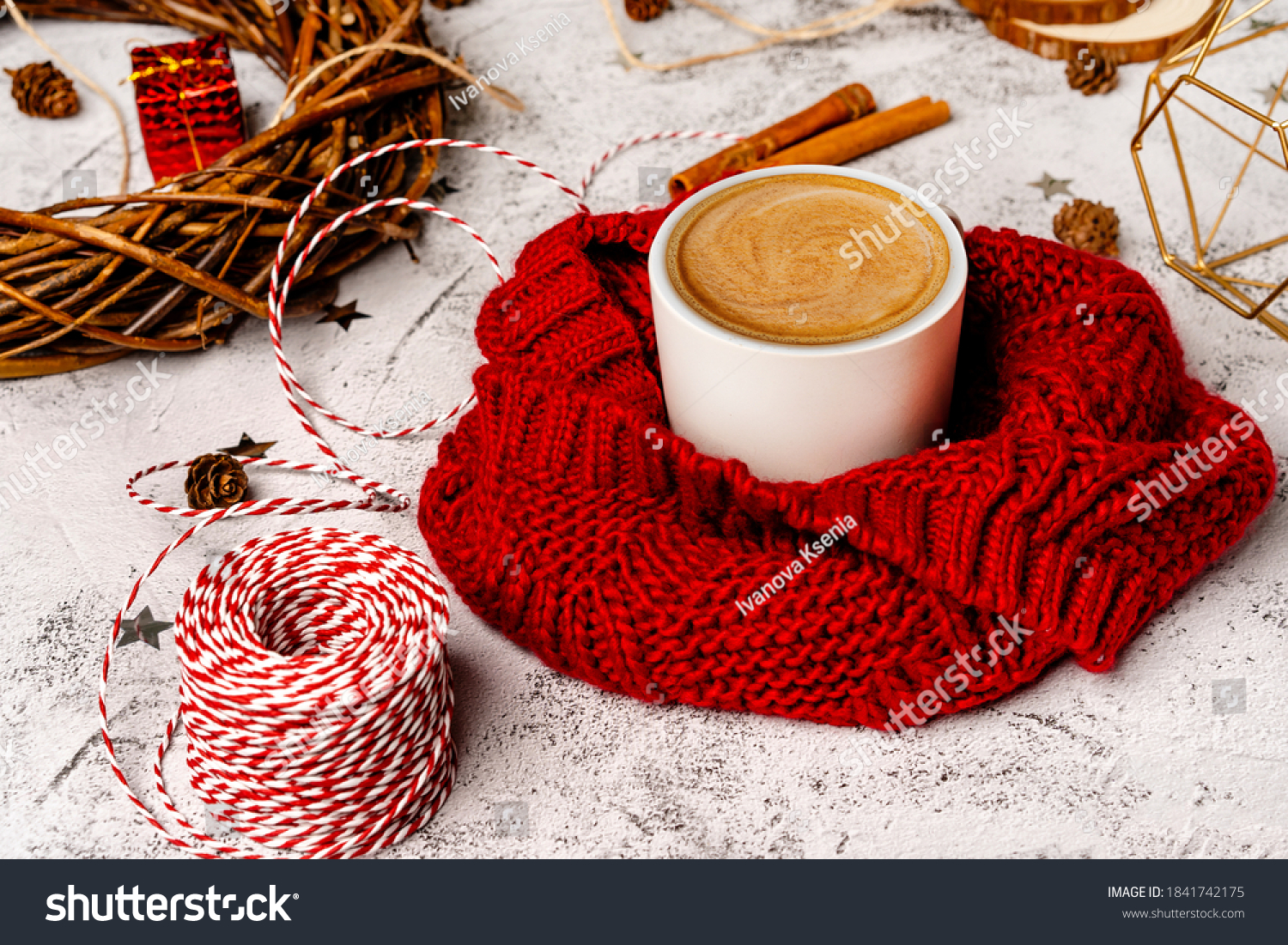 Coffee mug in a soft red winter scarf on a gray background with Christmas decorations. Christmas coffee break for home recreation. The view from the top