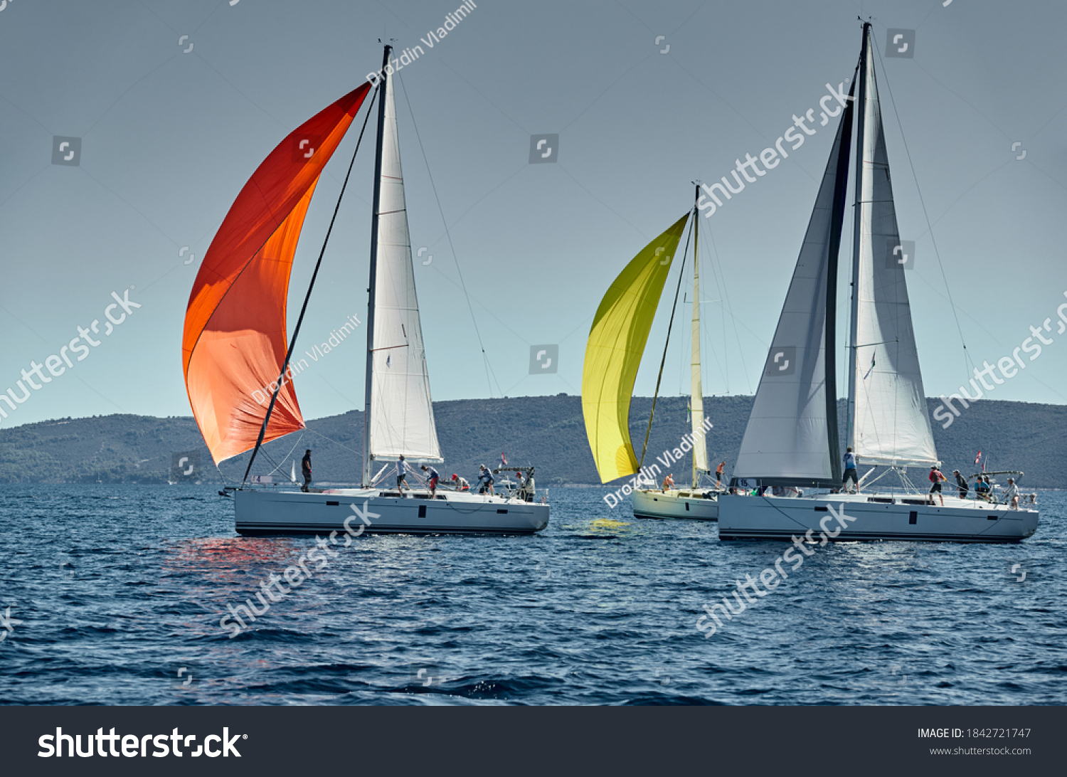 Sailboats compete in a sail regatta at sunset race of sailboats reflection of sails on water multicolored spinnakers number of boat is on aft boats island is on background clear weather