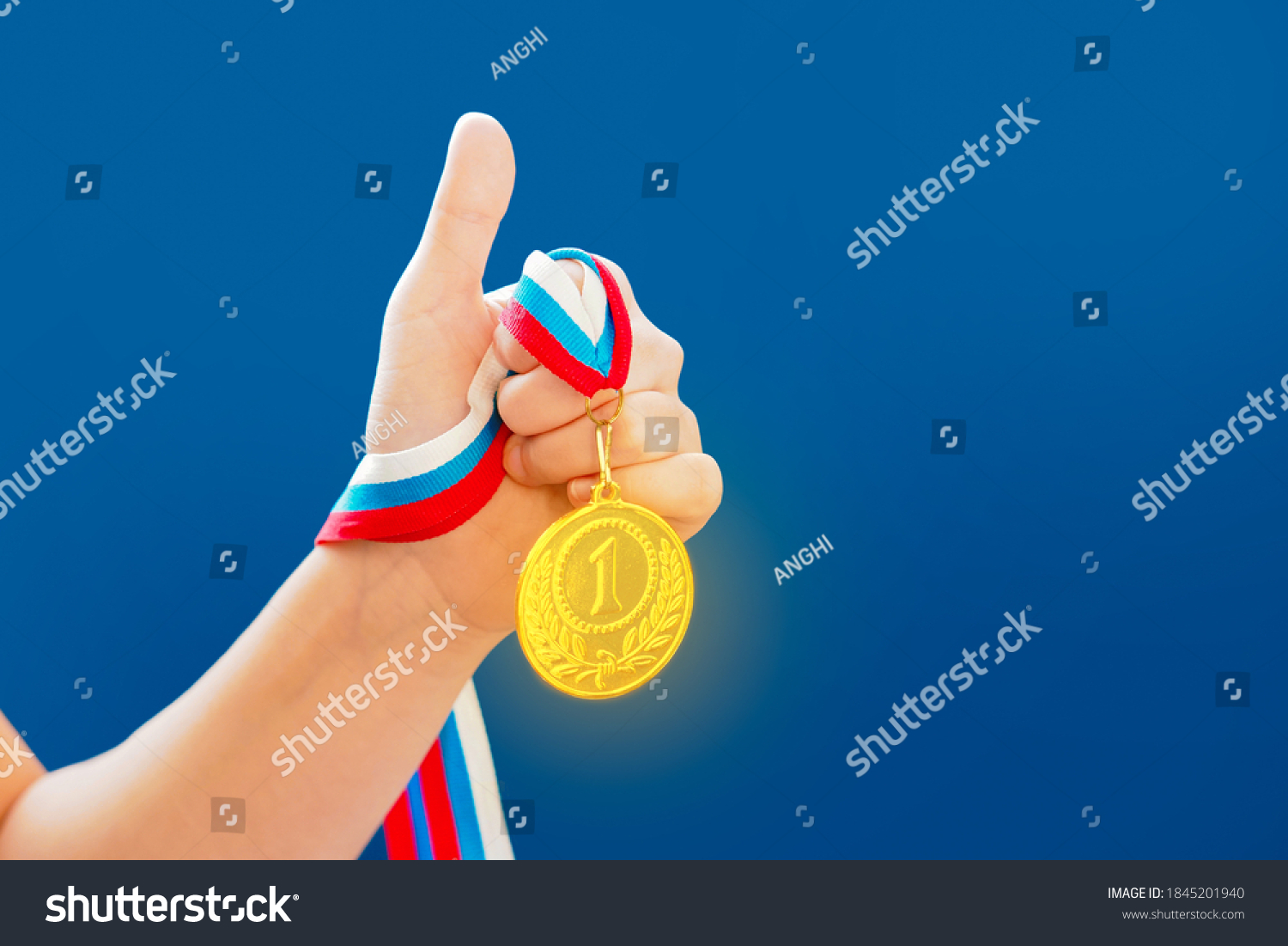 Award and victory concept. Woman hand raised with a thumb up sign  holding gold medal  blue background  copy space for text. First place in competition
