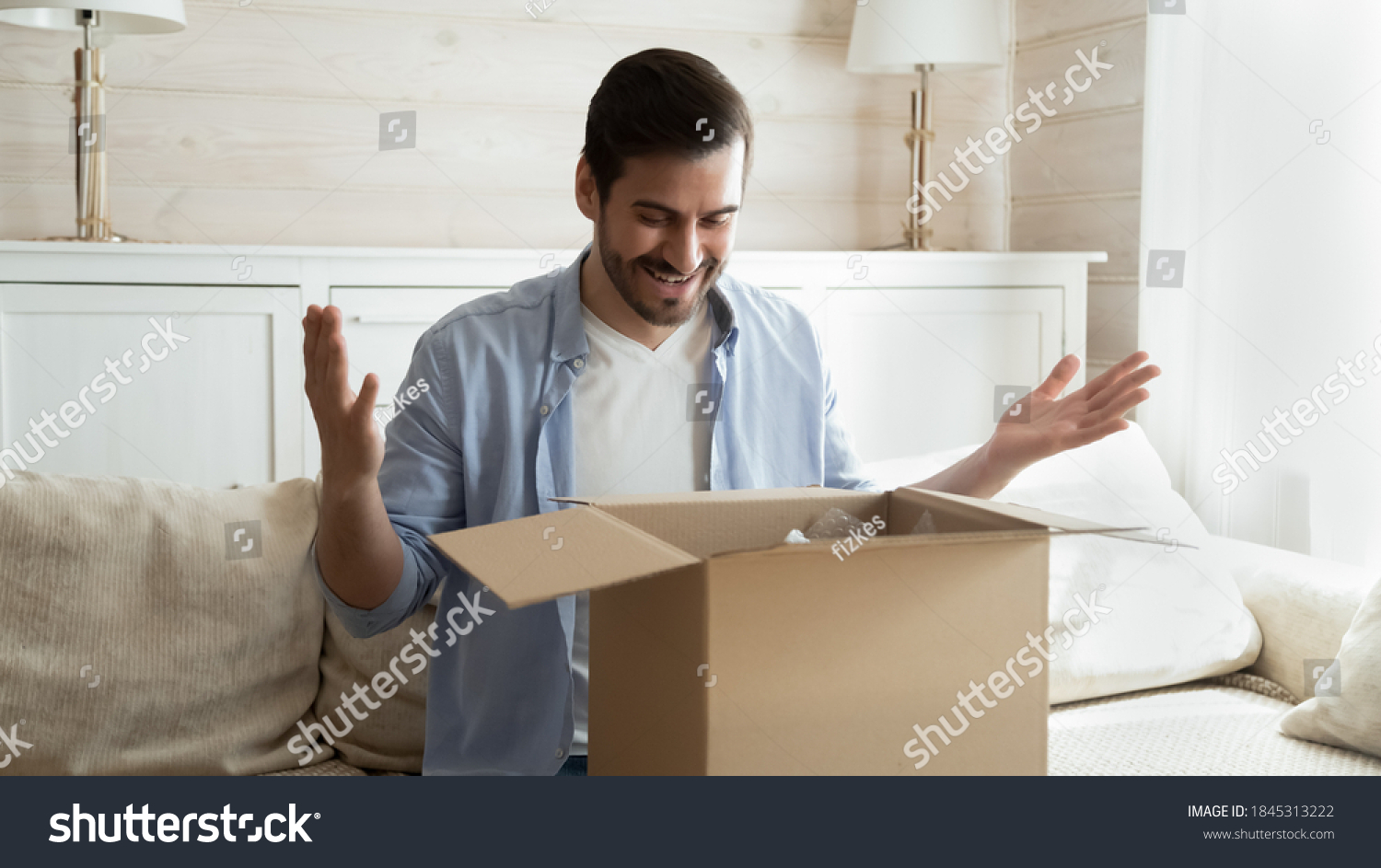 Just what I wanted! Glad happy young man sit on couch opening box with gift surprise send by beloved person millennial vlogger recording promotional video of unpacking parcel with sponsor products