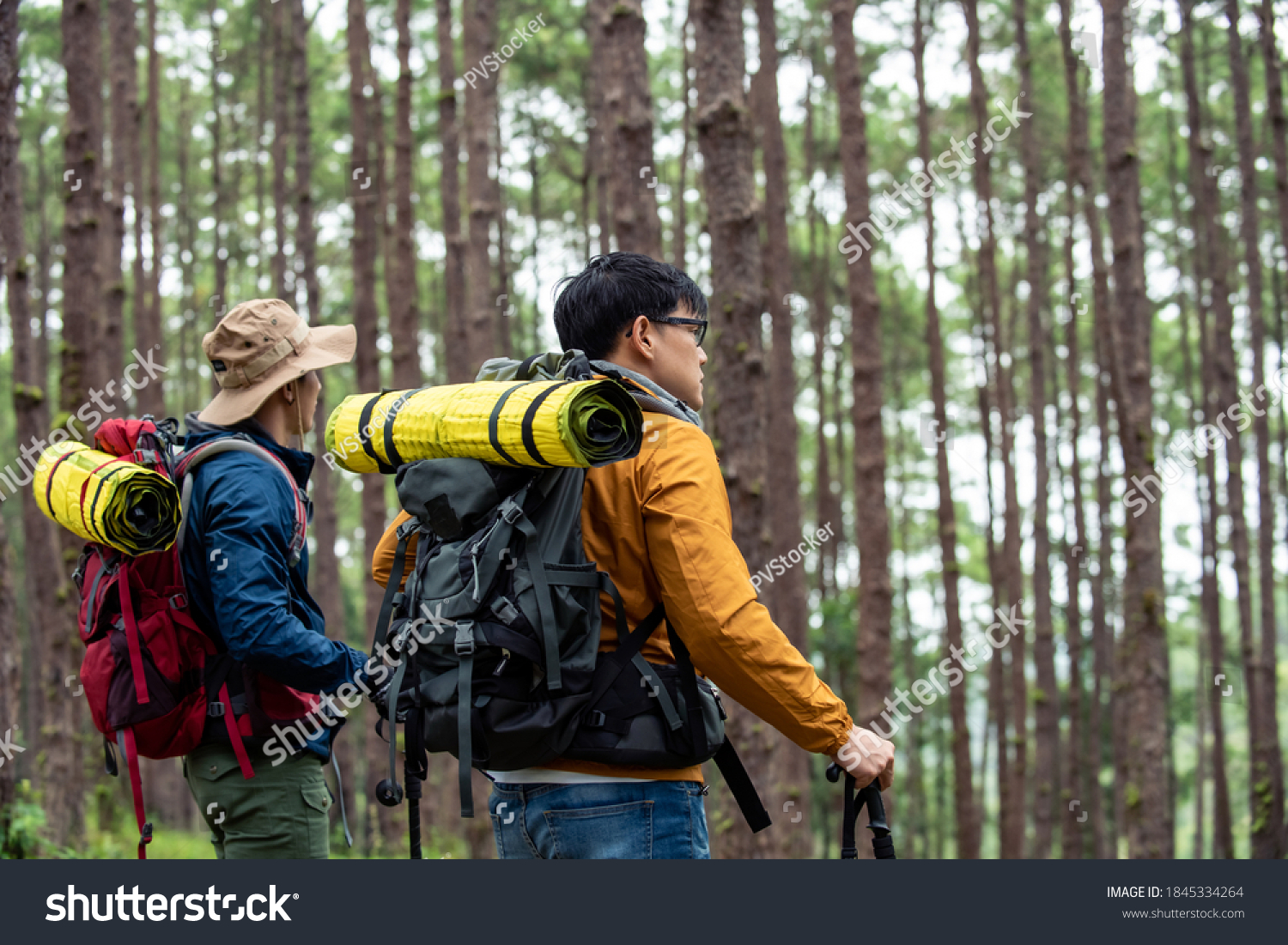 Portrait of Two Asian man friends hiking together in autumn forest. Male backpacker walking on mountain trail. Healthy outdoor lifestyle friendship and holiday vacation concept.