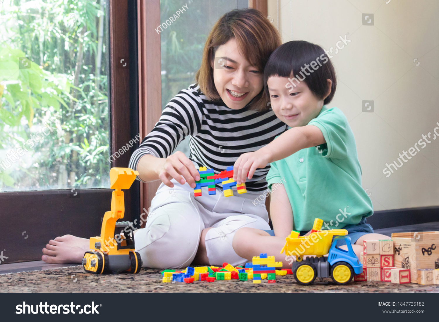 Asian mother is playing block toys with son while construction car truck and wooden ABC block are on the floor. Quality family time concept.