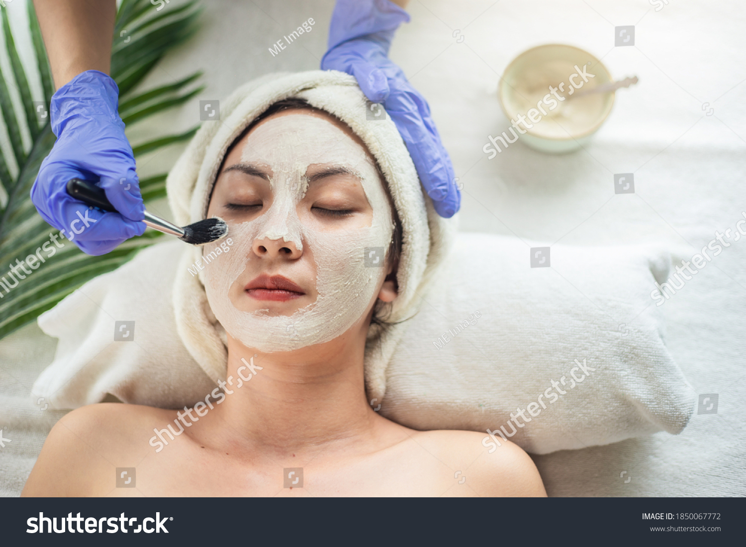 Asian woman getting facial face care by beautician at spa salon  Closeup face female applying clay mask by beautician. Young woman beauty treatment.