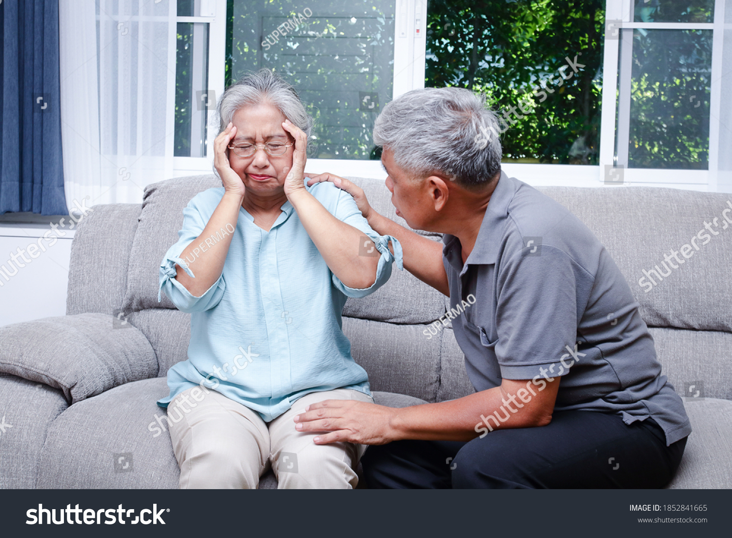 An elderly Asian couple sitting on the sofa at home A husband takes care of a wife who has a headache and is sick. Senior health concept