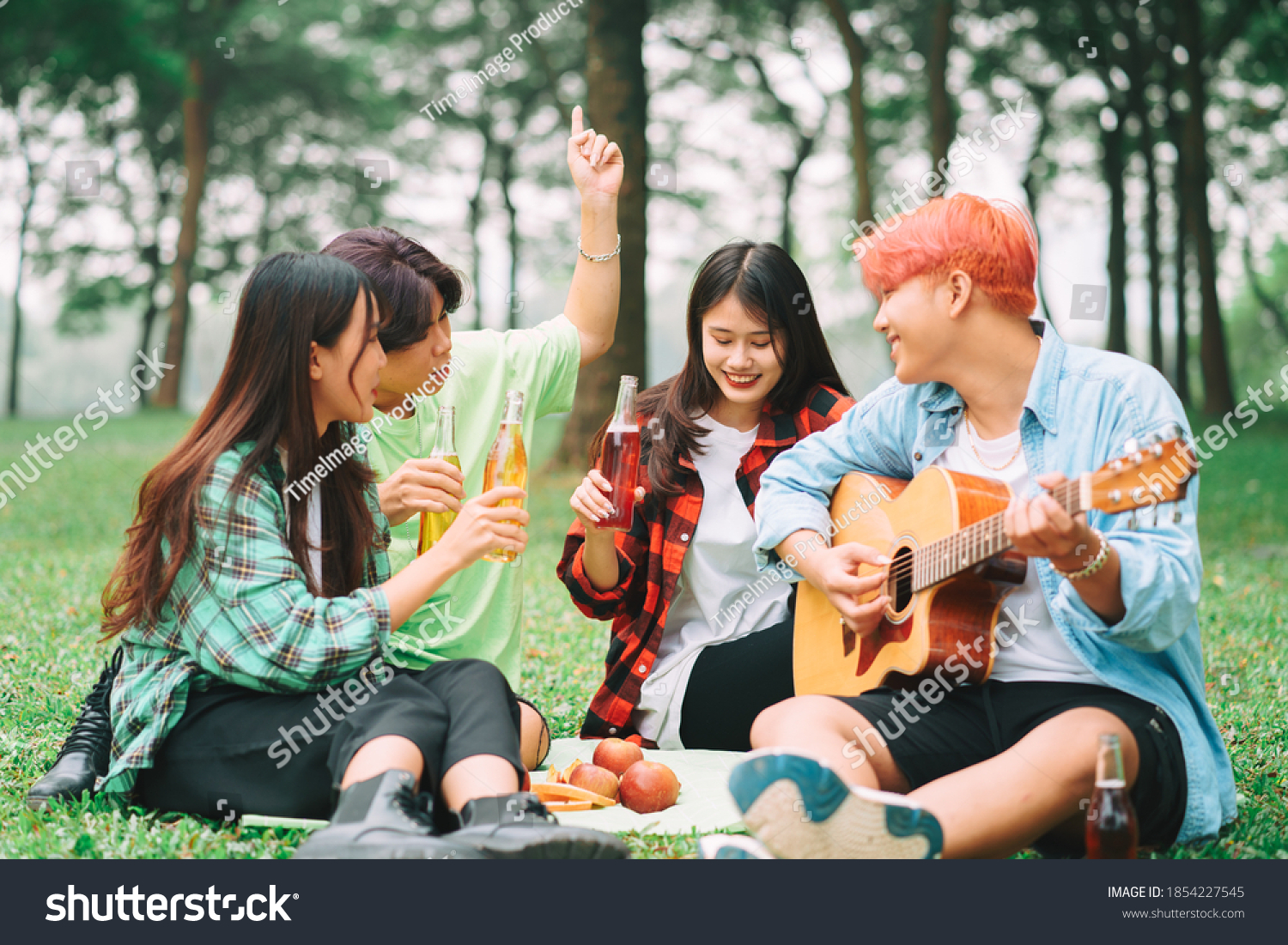 group of happy Asian young people sitting on the guitar and singing in the park
