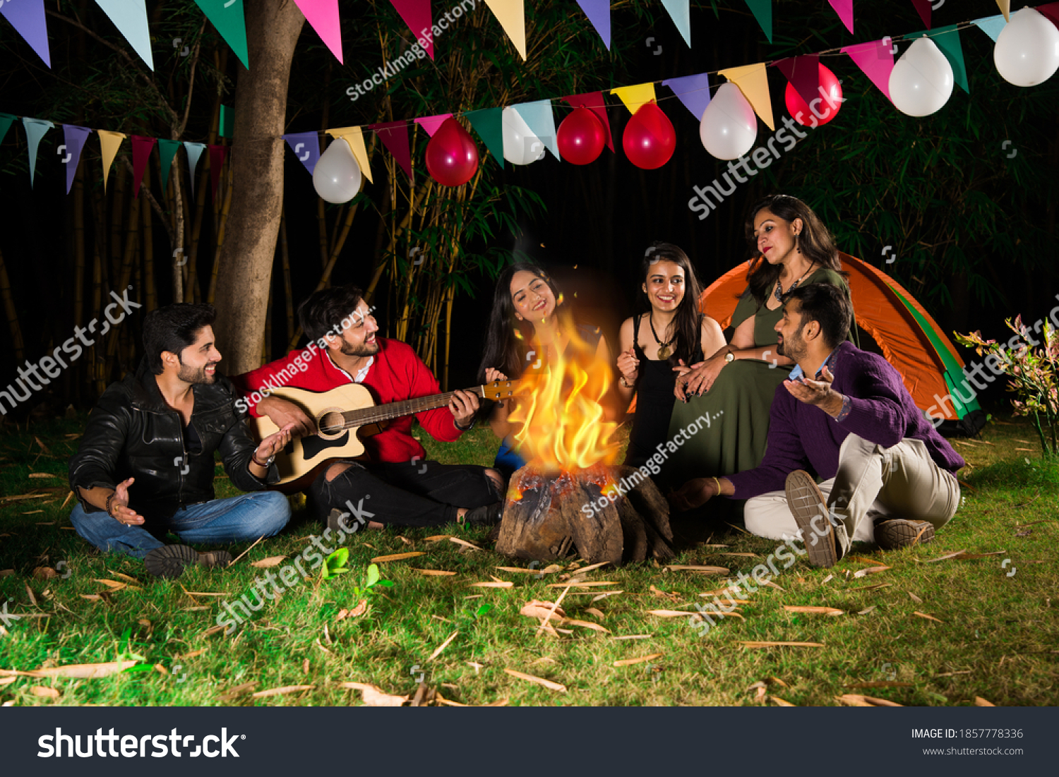 Happy Indian asian friends playing music and enjoying bonfire or campfire in nature
