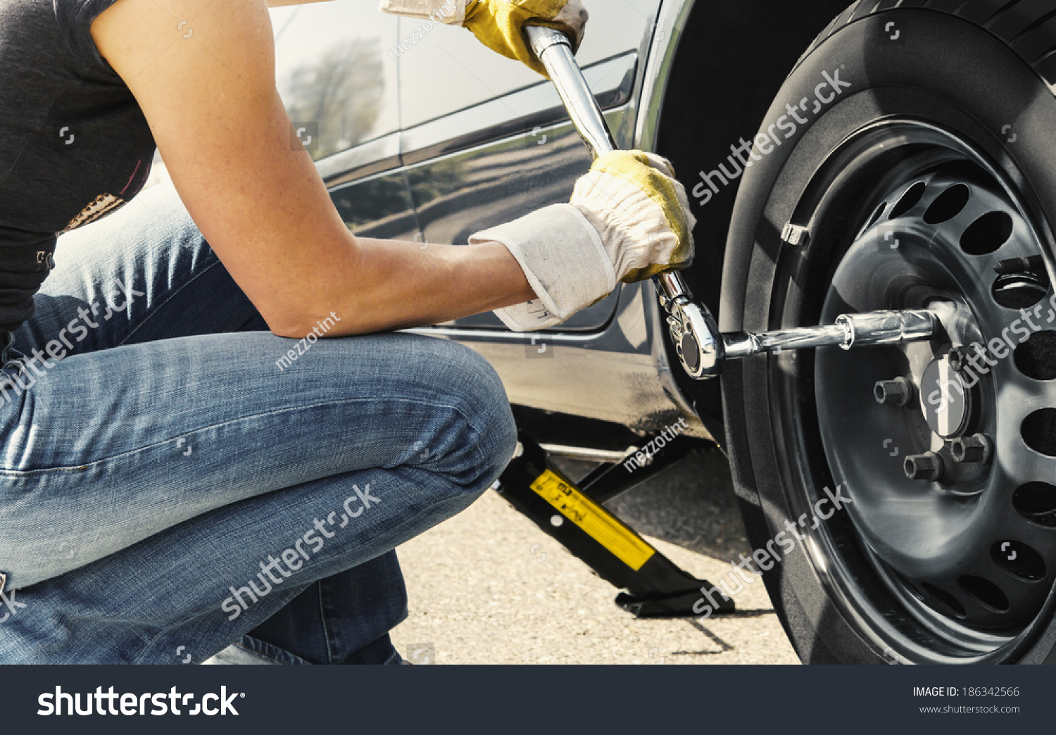 Woman is changing  tire of her car with wheel wrench.