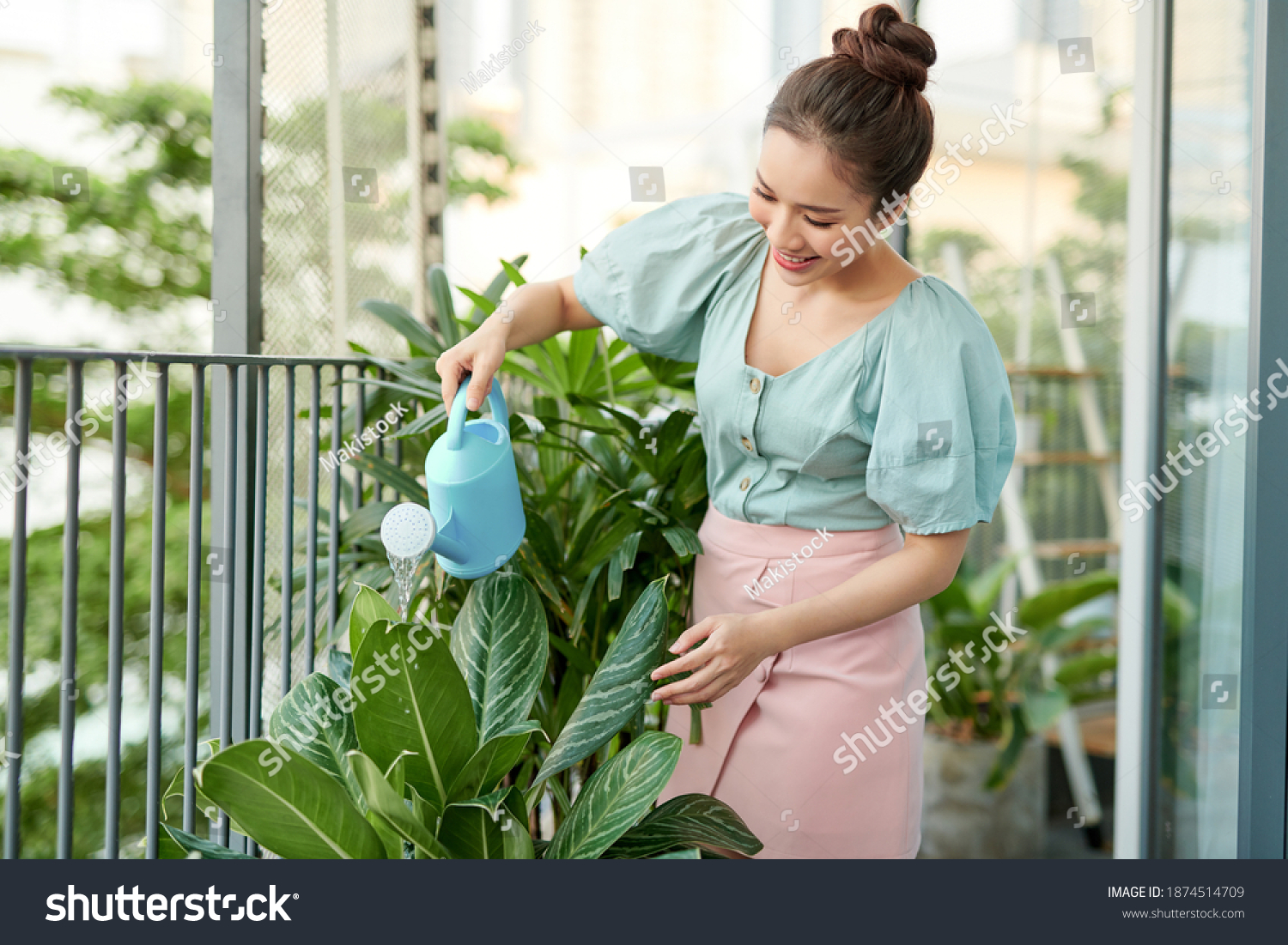 Happy Young Asian Woman housewife Watering flowers On Balcony.