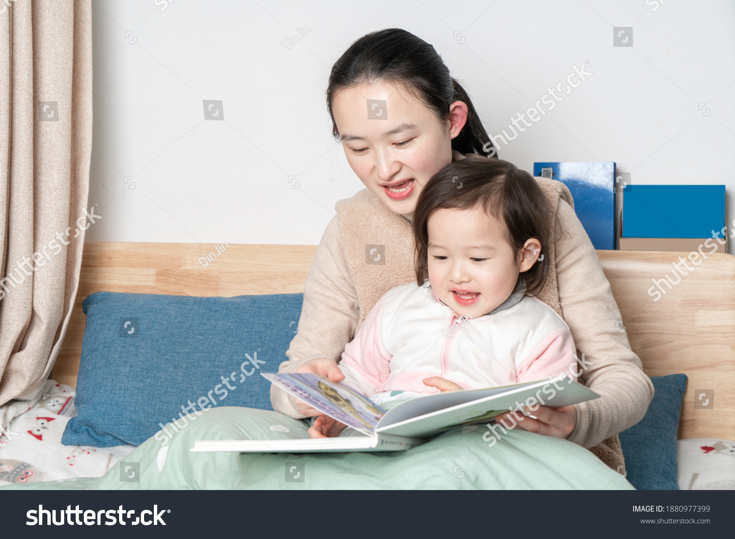 Mother and daughter sit on the bed reading together