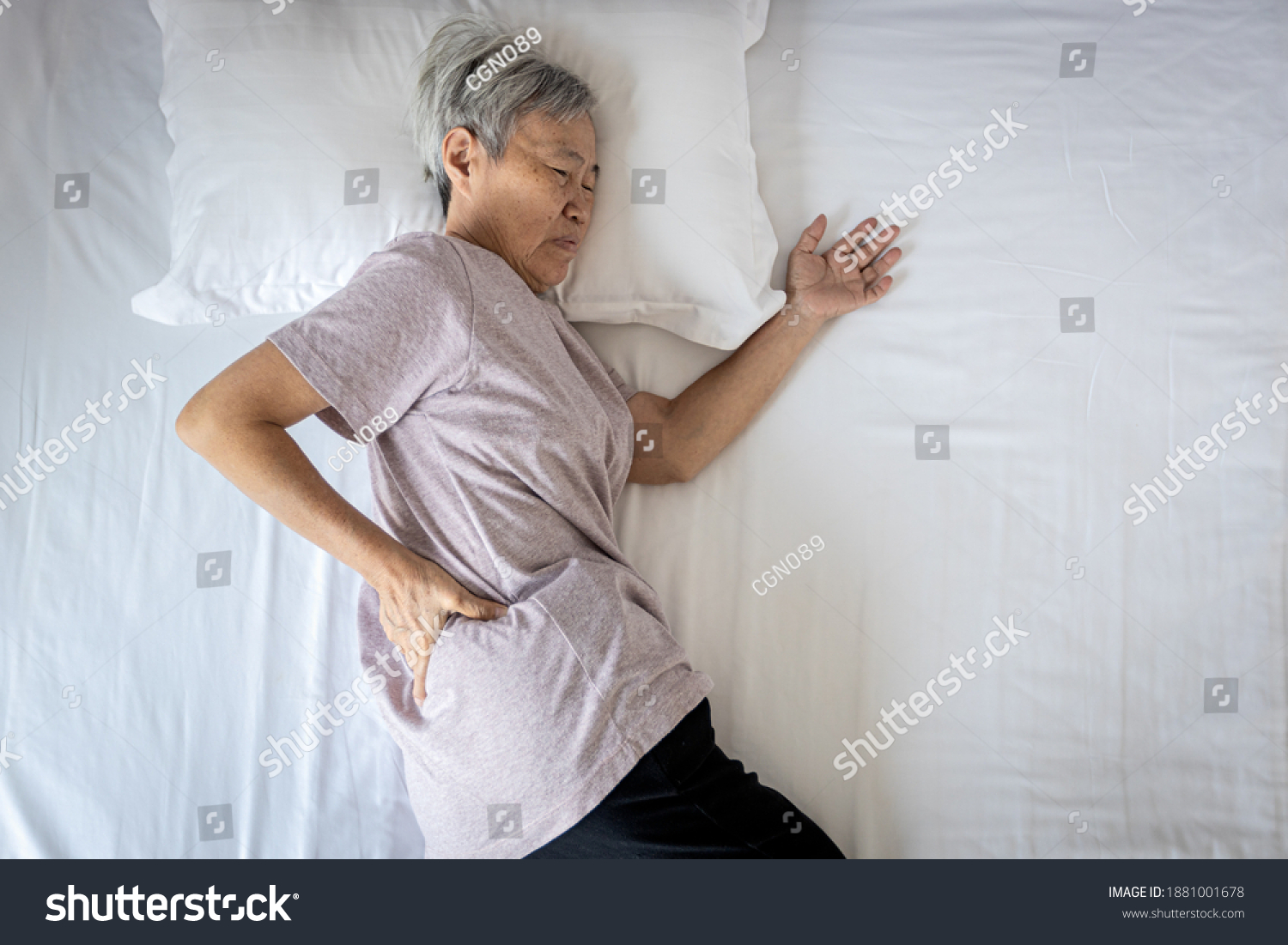 Sad asian senior woman touching hip on her bed problem of pain while sleep feel backache discomfort female old elderly suffering from sudden back pain caused by uncomfortable mattress in the bedroom