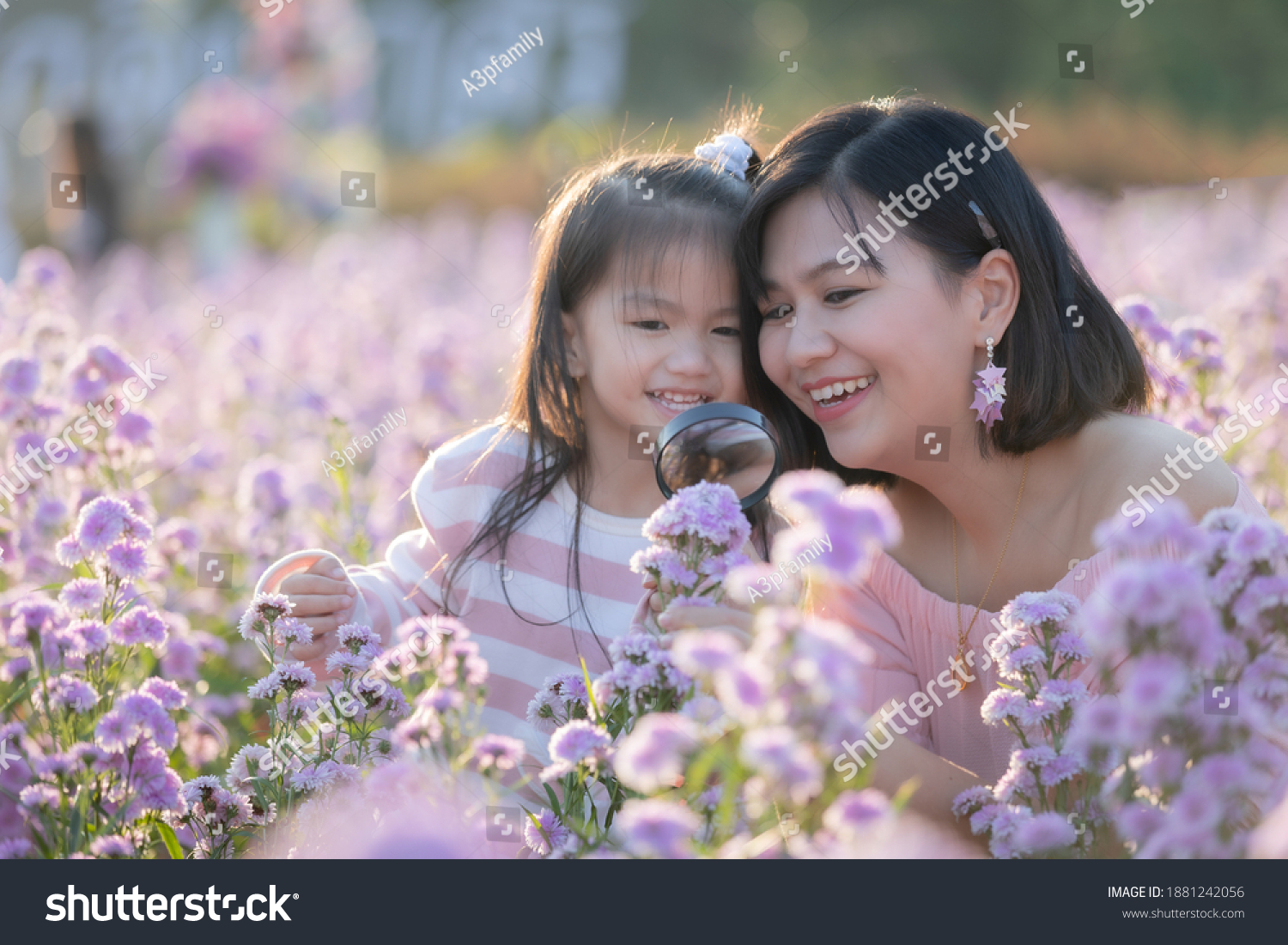 Cute asian child girl and her mother enjoying with beautiful flower together and little girl holding magnifier looking on flower with fun and curiously in the flower garden.