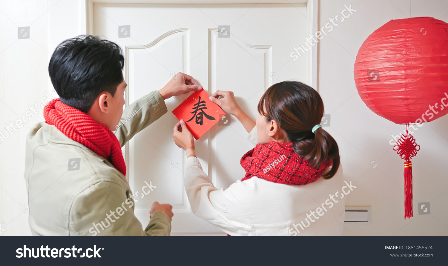 rear view of asian young couple paste up character of word meaning spring on the door to celebrate chinese new year