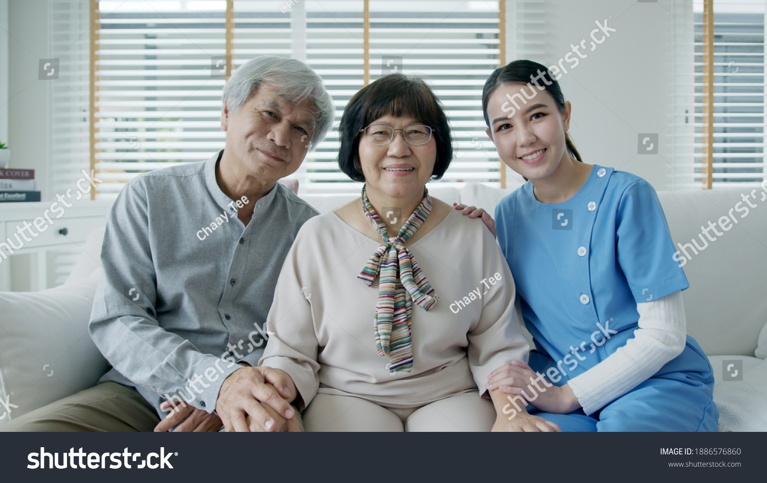 Portrait group shot of happy senior asian couple with in home nursing care sitting smile at sofa couch looking at camera with enjoy retirement or quarantine time. Asia adult older people lifestyle.