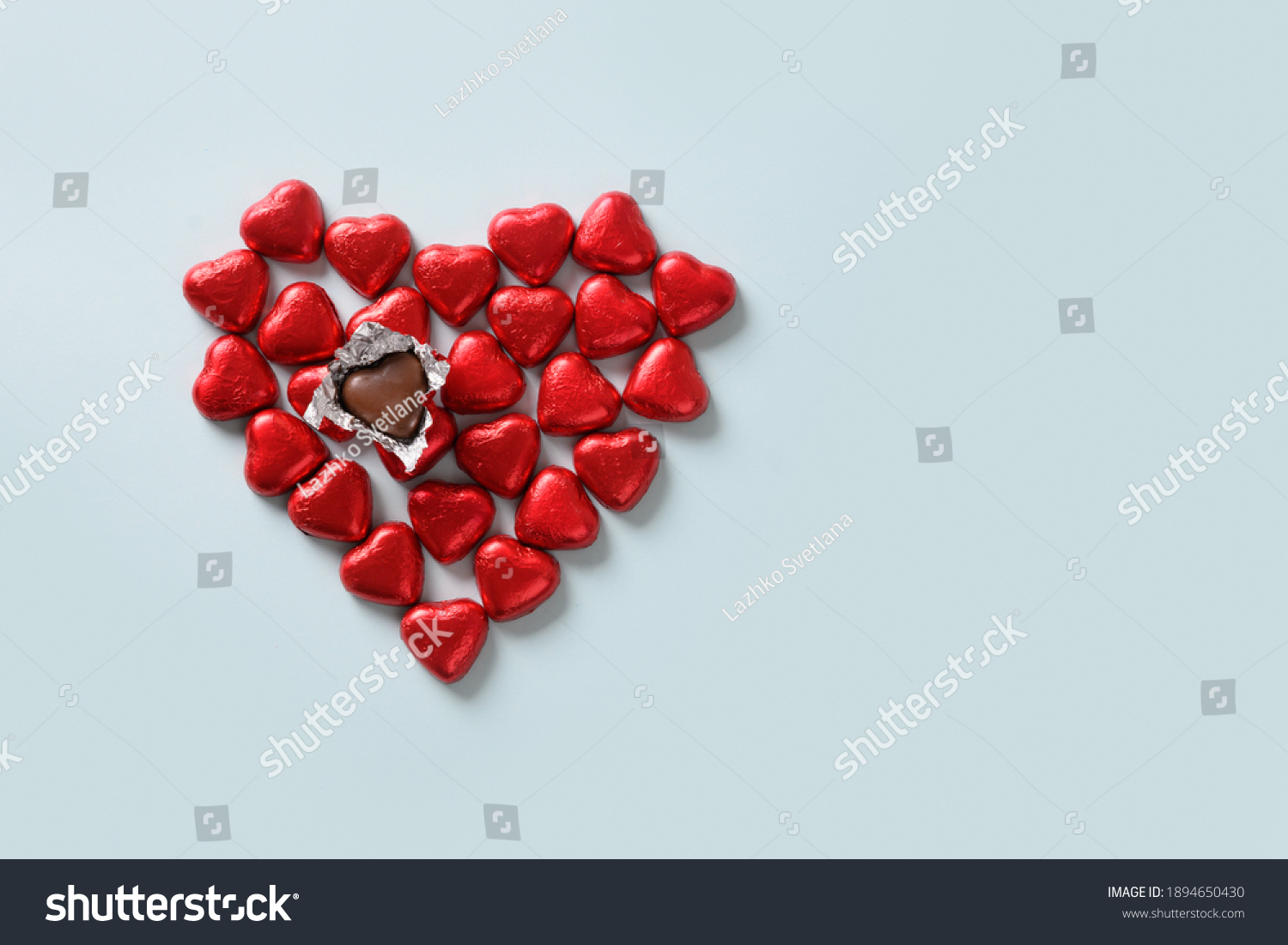 Red chocolate sweets as heart on blue background. Valentine's day concept.