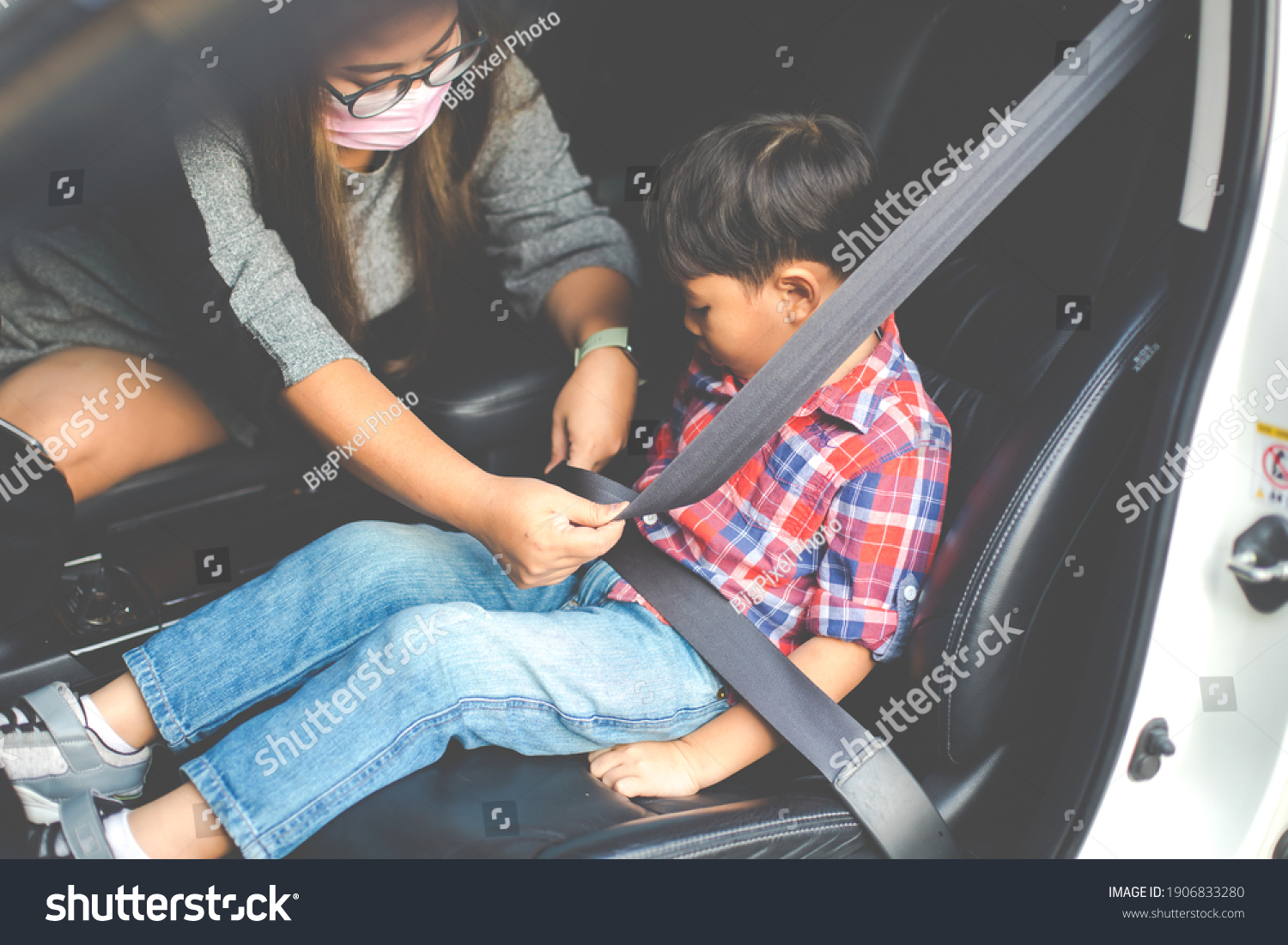 Asian fat woman fastening child with safety seat belt in car.