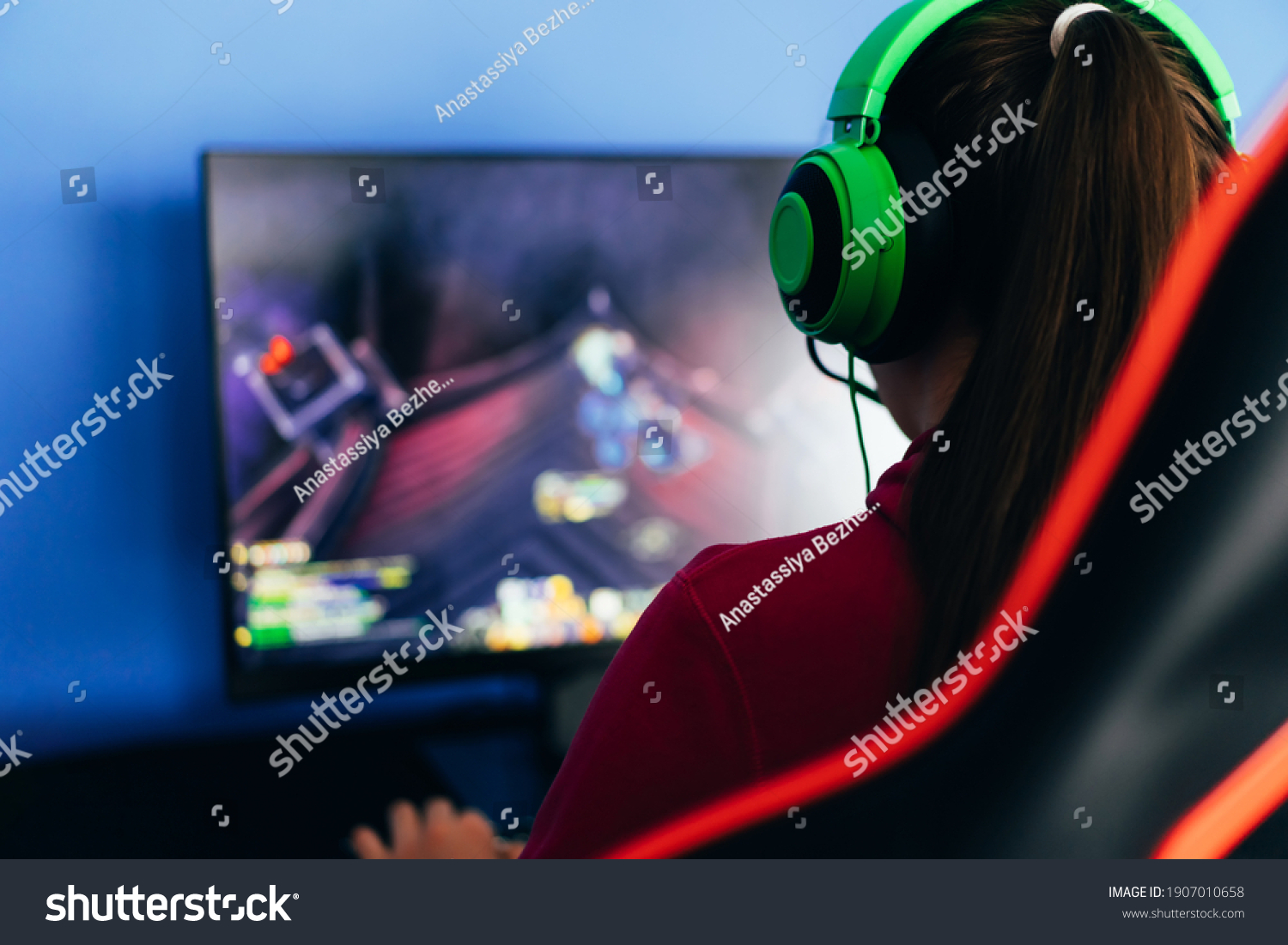 A young girl playing a computer game on professional armchair against monitor in green headphones live stream esports.