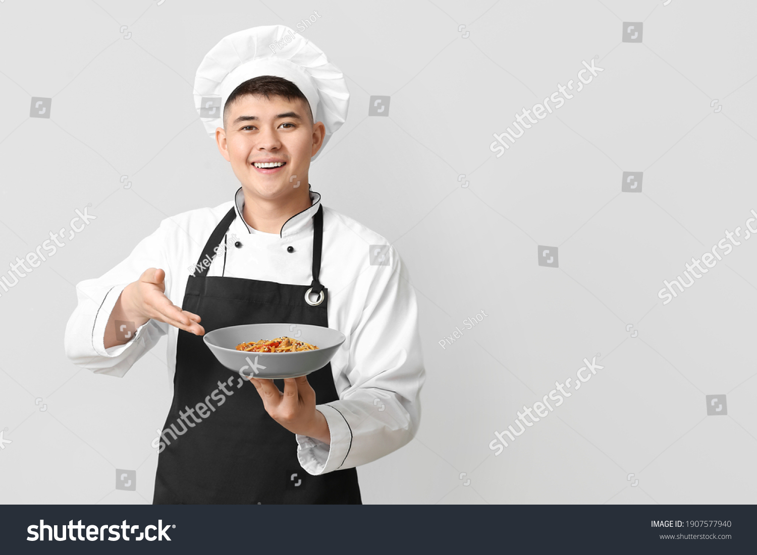 Handsome Asian chef with dish on grey background