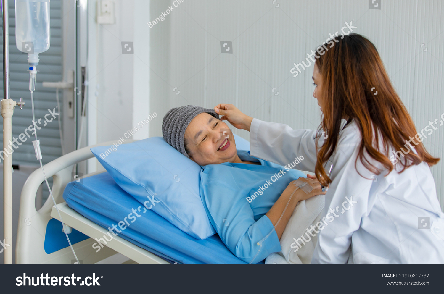 Older Asian woman patient covered the head with clothes effect from chemo treatment in cancer cure process talking to a female doctor.