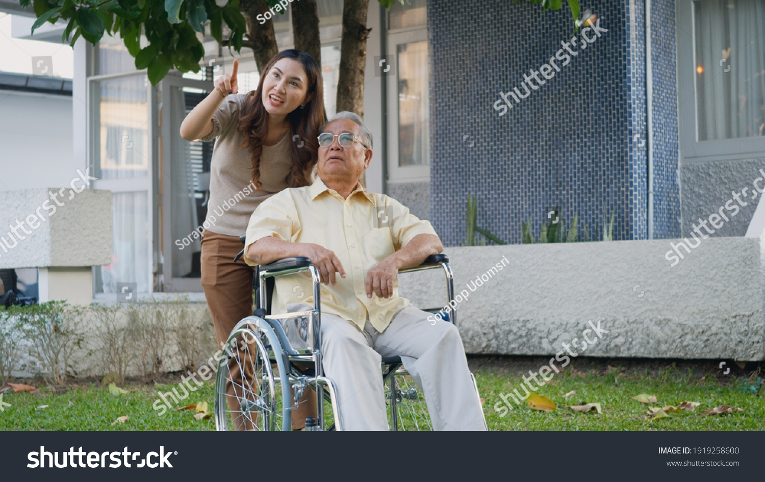 Disabled senior man on wheelchair with daughter Happy Asian generation family having fun together outdoors backyard Care helper young woman walking an elderly man smiling and laughed