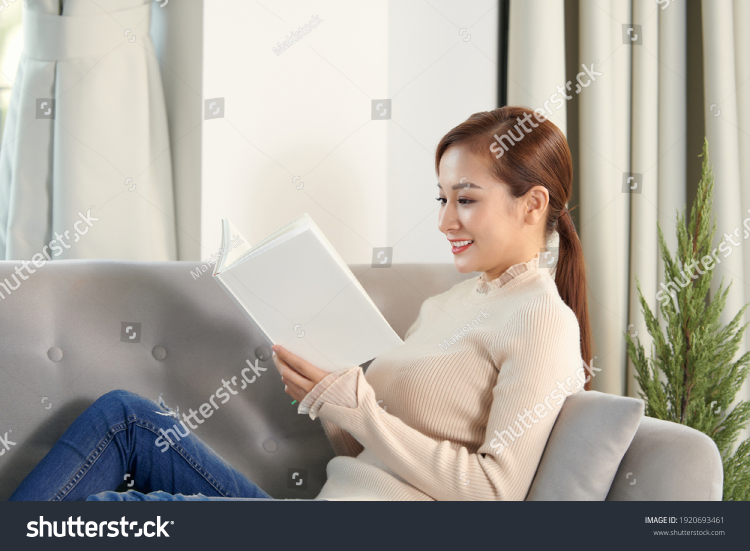 Young beautiful woman sitting on the sofa reading a book enjoying her tea in living room at home