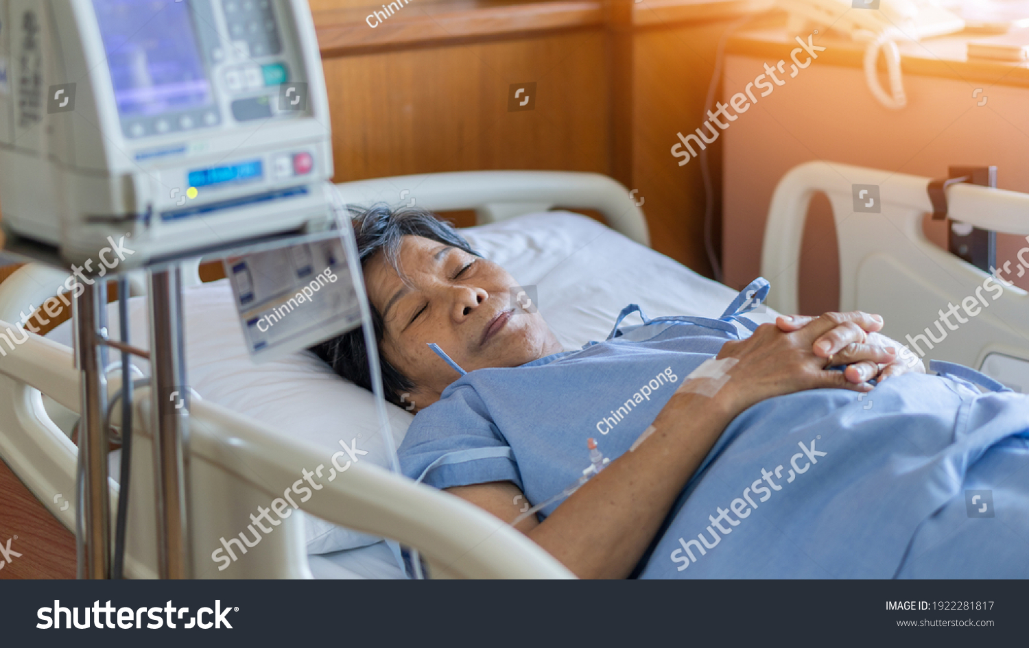 Hospitalized elderly patient woman laying on bed in hospital ward room with iv medical infusion pump infusing saline solution fluids medication for health treatment