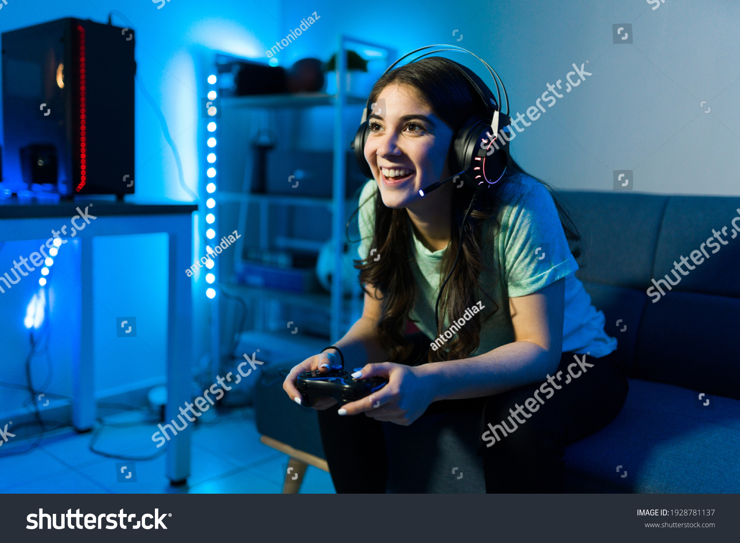 Happy female gamer smiling while playing and winning in a video game with a remote controller. Young woman sitting on the couch in her bedroom with neon led lights