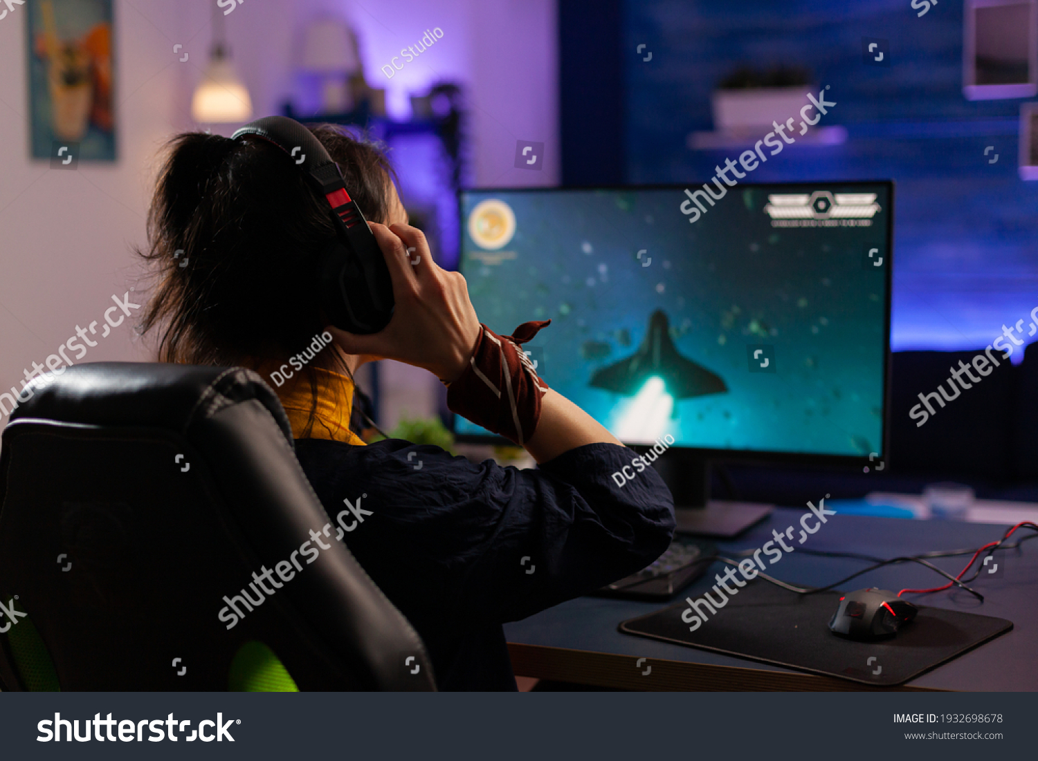 Focused Gamer puts professional headphones and playing space shooter videogames use modern equipment for digital tournament. Pro player sitting on gaming chair streaming video games using RGB keyword