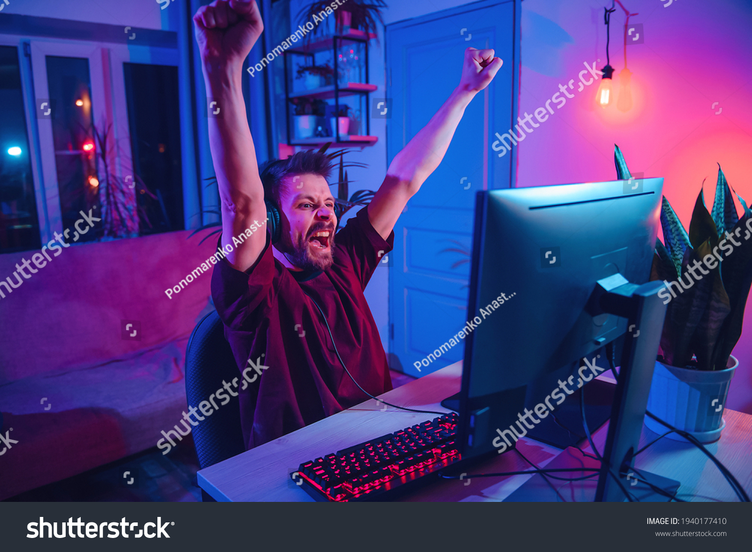 Young man plays computer games at home. Neon streamer studio. The guy with the headphones is having fun on the Internet.