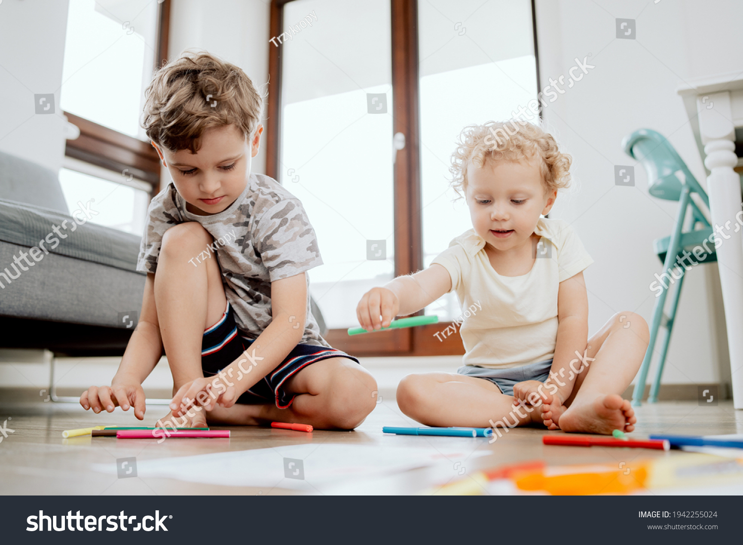 Siblings drawing with colored markers while lying on wooden floror at