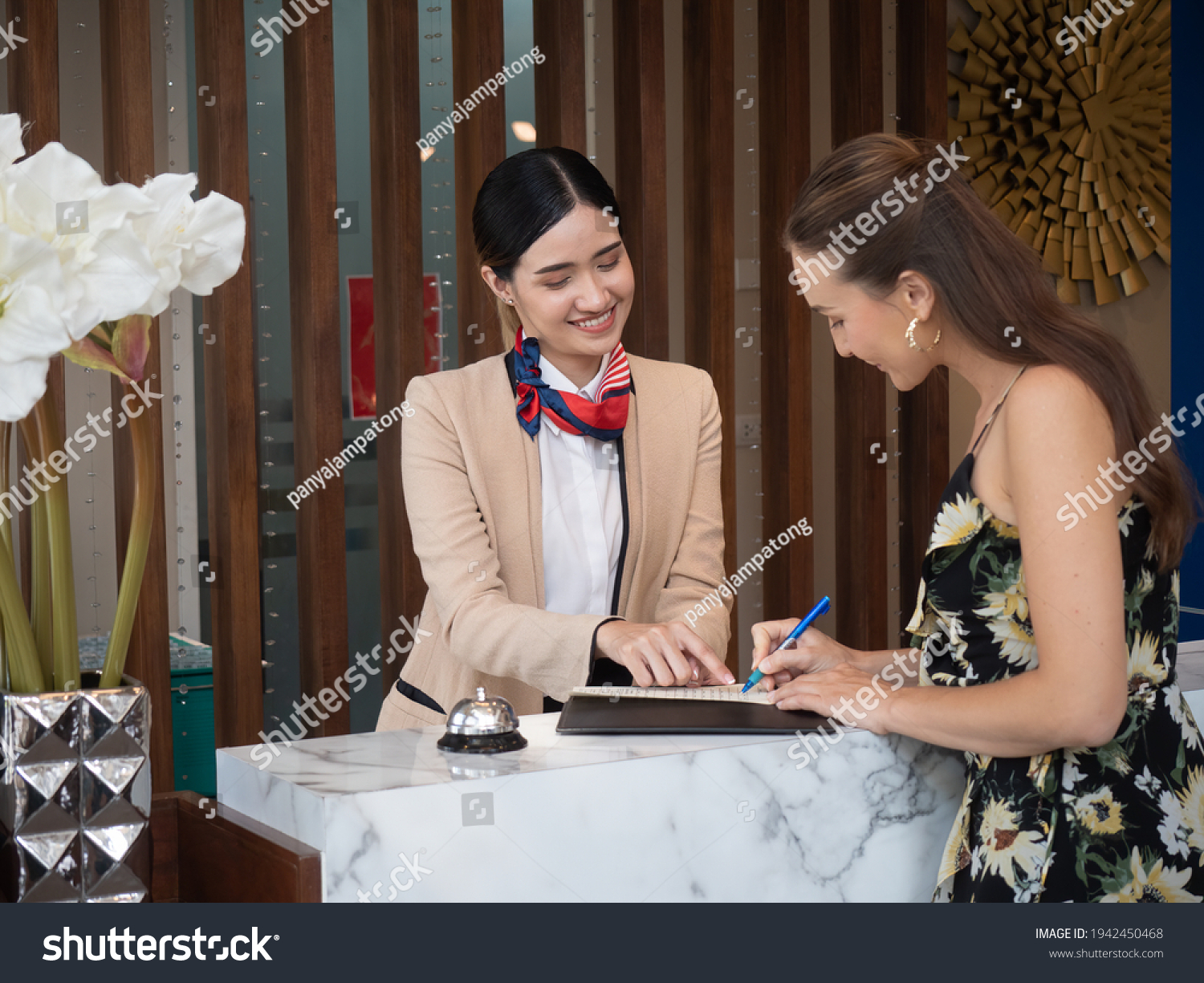 Young travelers talking and check-in register information with woman receptionist worker standing in counter hotel reception counter desk at lobby modern hotel.