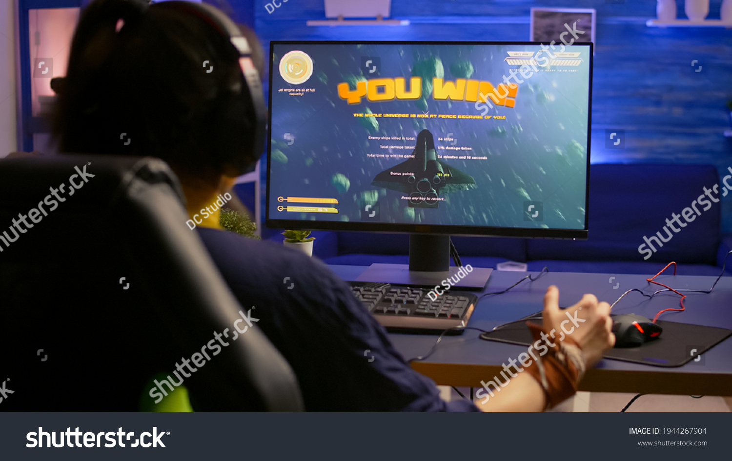 Excited pro gamer with professional headphones making winner gesture while playing space shooter video games. Player streaming digital games during online competition using RGB system desktop