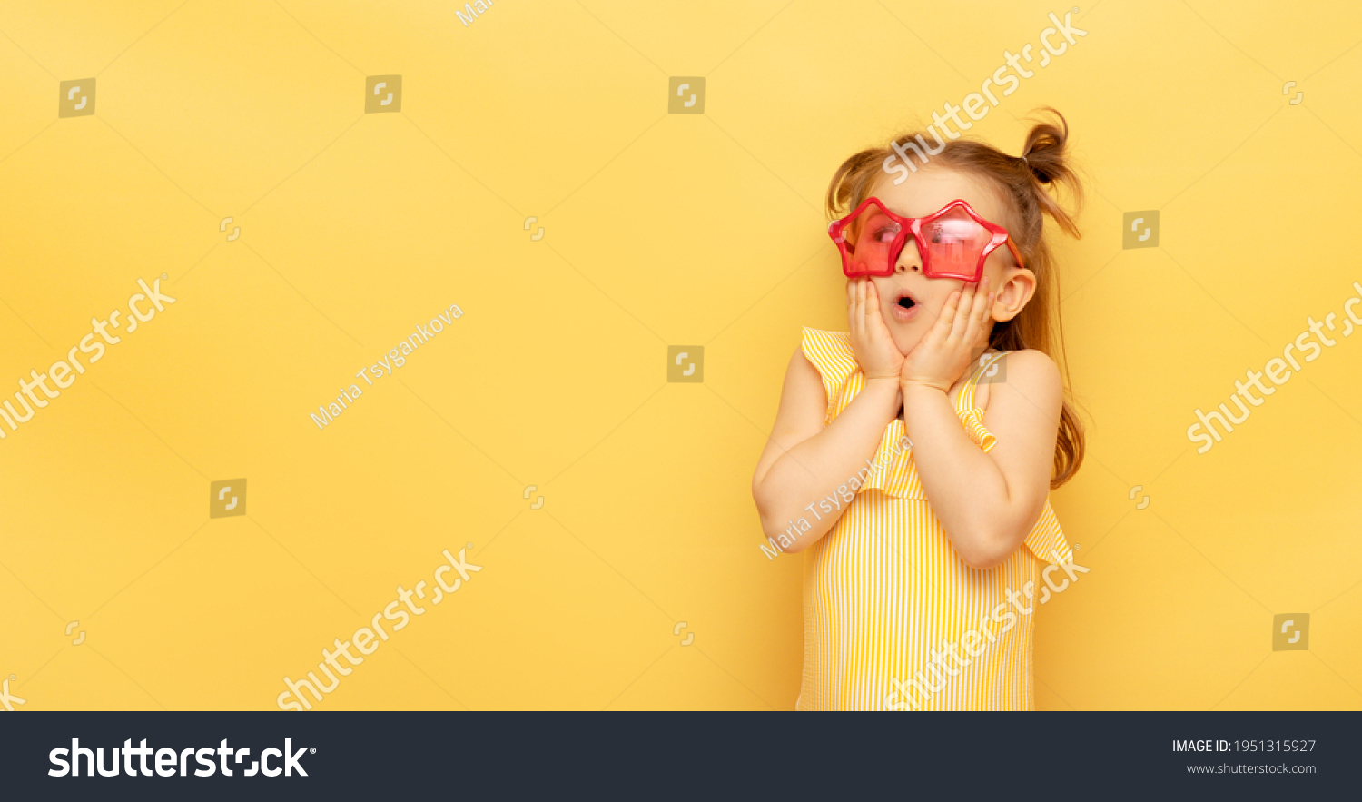 Little child girl in striped swimsuit and red funny summer sunglasses surprised expression looks at camera posing on yellow background studio portrait.Advertising of children's products and sale