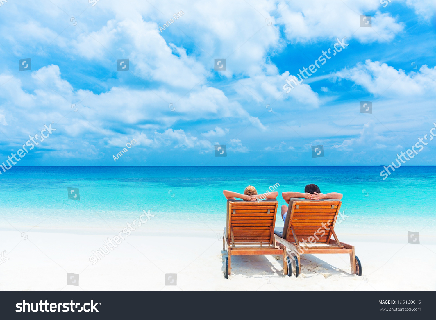 Two happy people relaxing on the beach sitting down on comfortable sunbed and taking sunbath rear view summer holidays concept