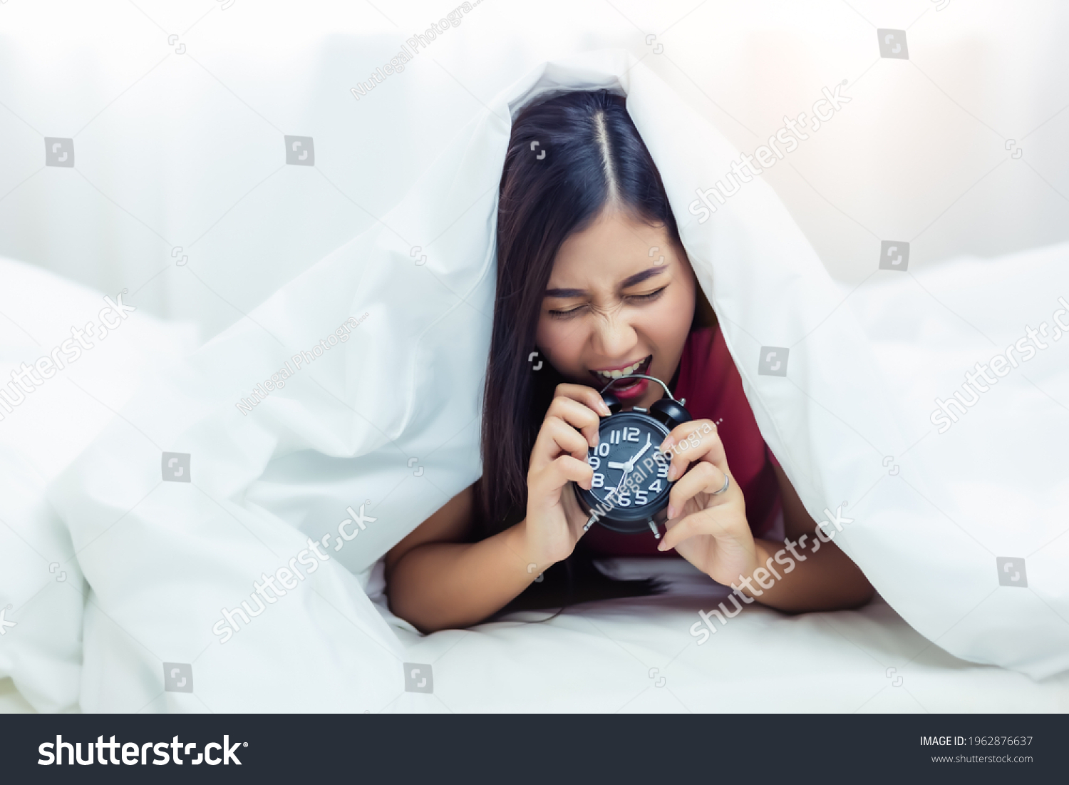 Lazy worker woman get frustrated of alarm clock Asian girl wake up late in Monday morning and she get angry when she wake up so late Female will go to work running late She biting alarm clock at bed